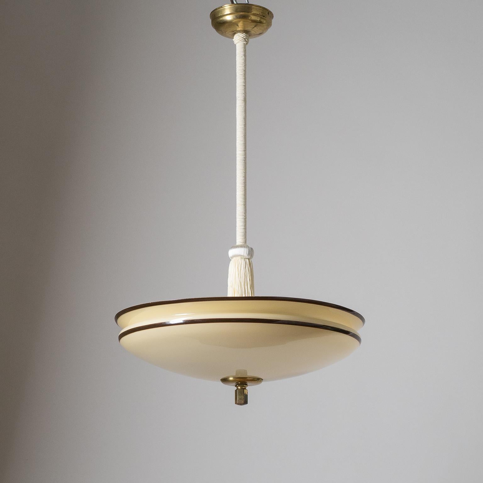 Art Deco pendant from the 1930s with an enameled glass diffuser. The shallow bowl shaped glass is sand-colored with a white inner casing and has two dark brown stripes painted along the rim. Stem with off-white passementerie trimmings and tassel.