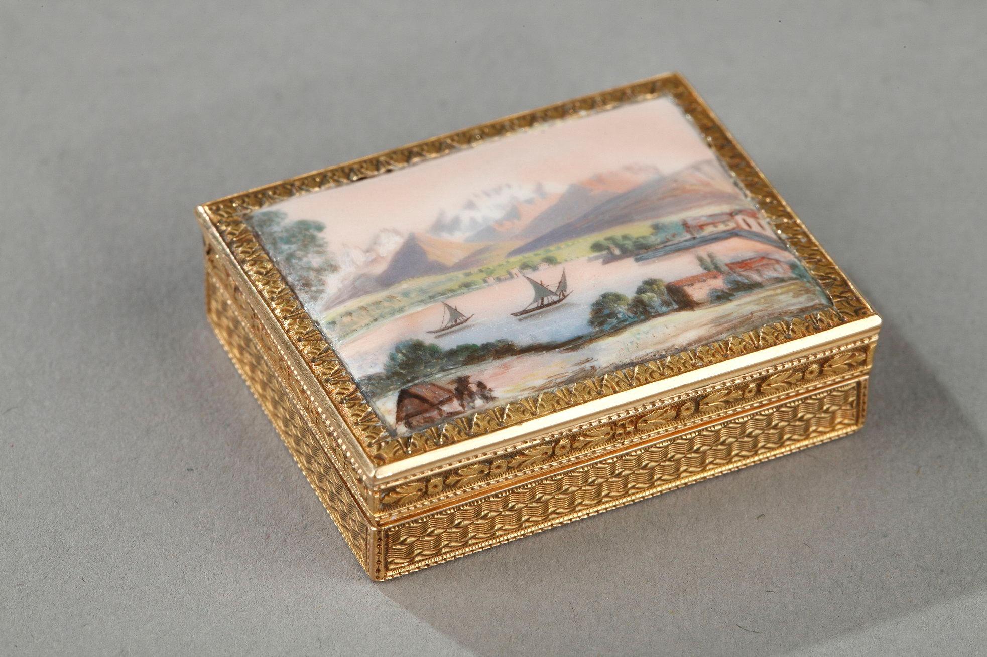 Rectangular, enameled gold vinaigrette. The hinged lid is decorated with enamel on gold and displays a view of an Alpine lake in front of a mountain range. The sides of the vinaigrette are embellished with finely etched waves and framed in a floral