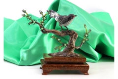 Enameled silver bird perched on a trunk with branches cut out on a wooden base