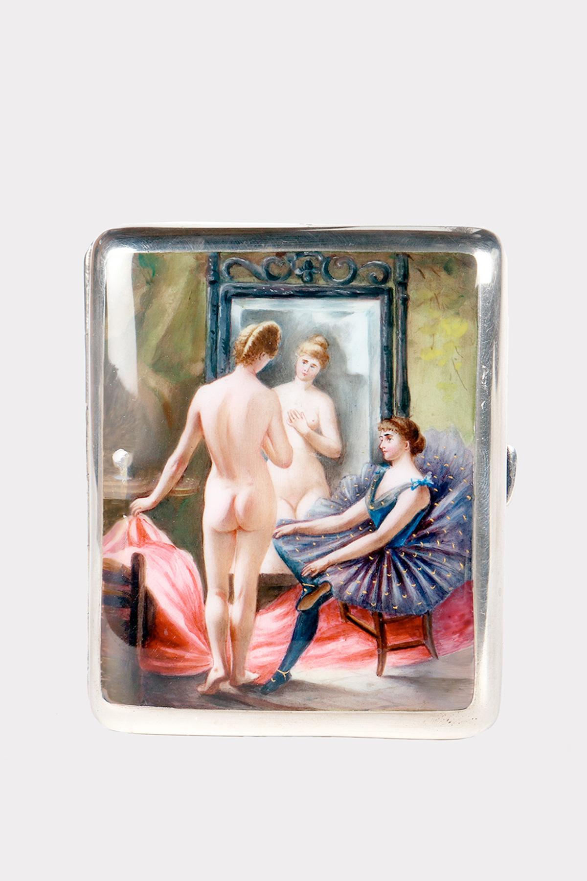 Scatola di sigarette in argento 900/1000. Il coperchio ha una superficie liscia su cui, in smalto, è raffigurata una scena erotica. Una donna nuda in piedi davanti a uno specchio che viene ammirata da una ballerina seduta che indossa un tutù blu. La