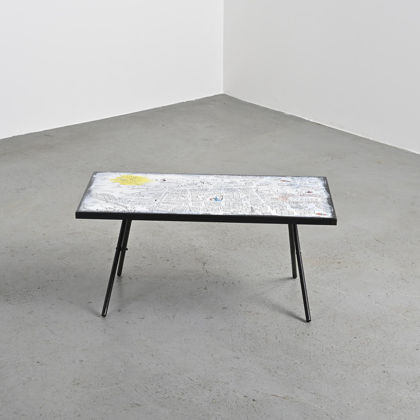 
Folding coffee table with black lacquered metal base, designed by Bernard Hesling circa 1970.

The rectangular enamelled metal top features a whimsical, stylized depiction of the city of Sydney, characteristic of the artist's playful and narrative