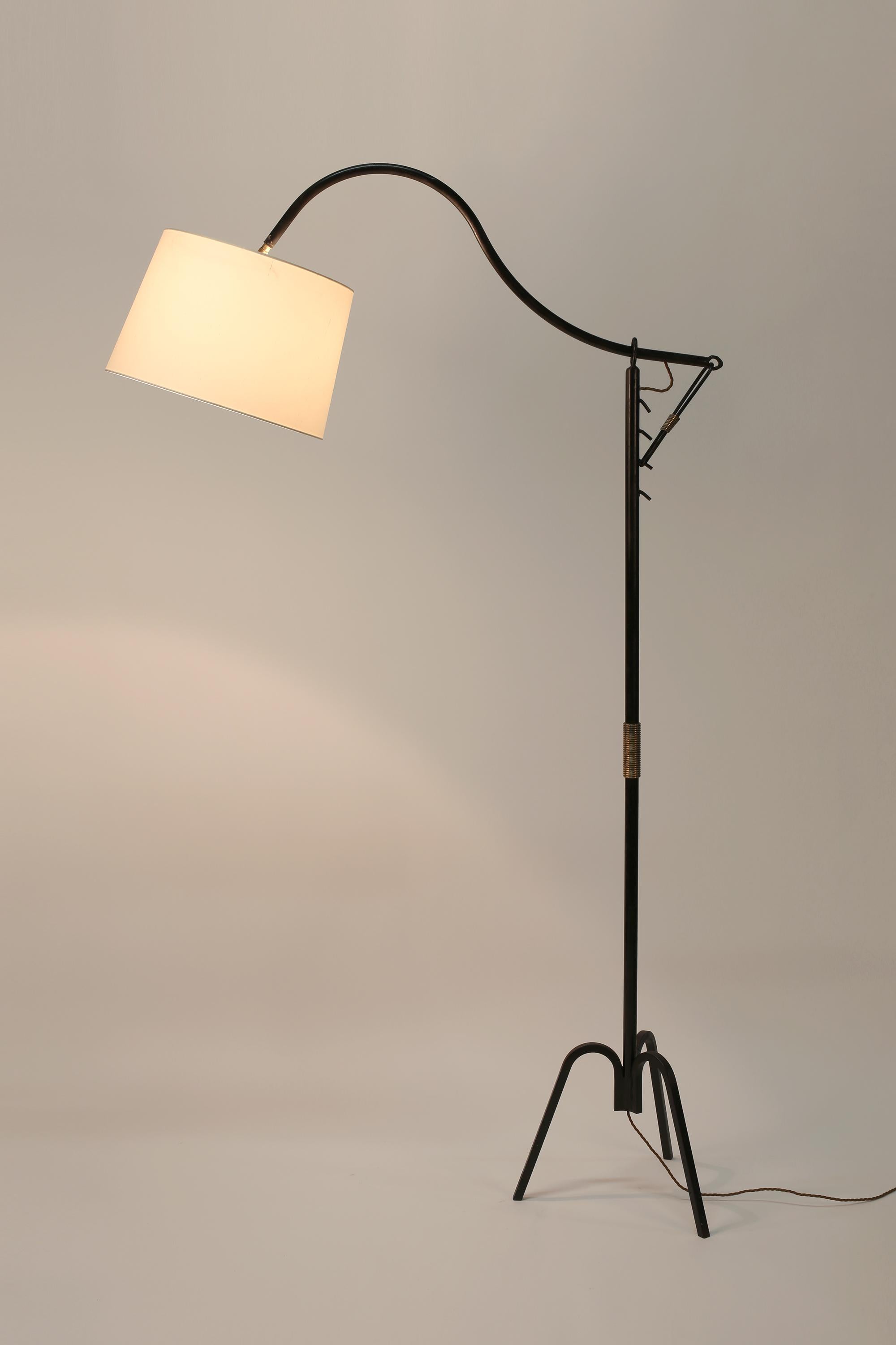A forged and enamelled iron floor lamp with decorative gilt bronze detailing, attributed to Jacques Adnet. Featuring unique ‘crémaillère’ height adjustment systems and tripod base. French, c. 1950. Supplied with an off-white dupion silk
