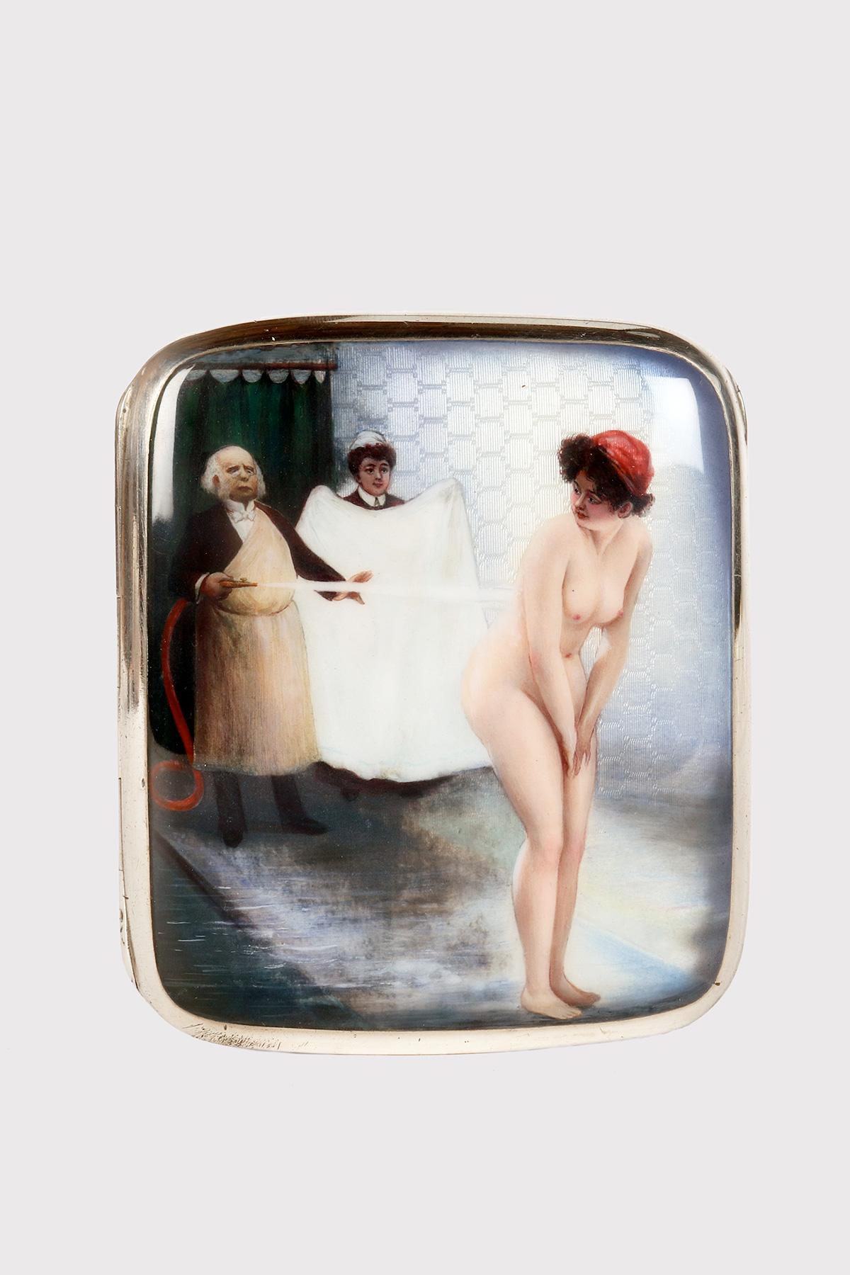 Scatola di sigarette in argento 900/1000. Il coperchio ha uno sfondo lavorato a guilloché sul quale, in smalto, è raffigurata una scena erotica con una donna nuda in piedi nel bagno che viene lavata da un uomo con un tubo. Una cameriera, con un