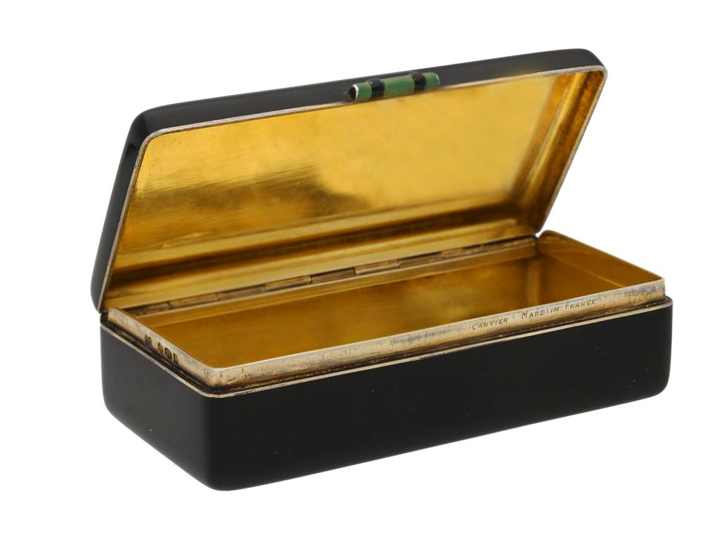 Enamelled silver gilt box, Cartier Paris, French, circa 1930. A silver gilt box in black enamel, the top centred with a stylized floral design, the hinged lid with a barrel shaped green and black enamel latch, approximately 7.6cm in length, 3.7cm