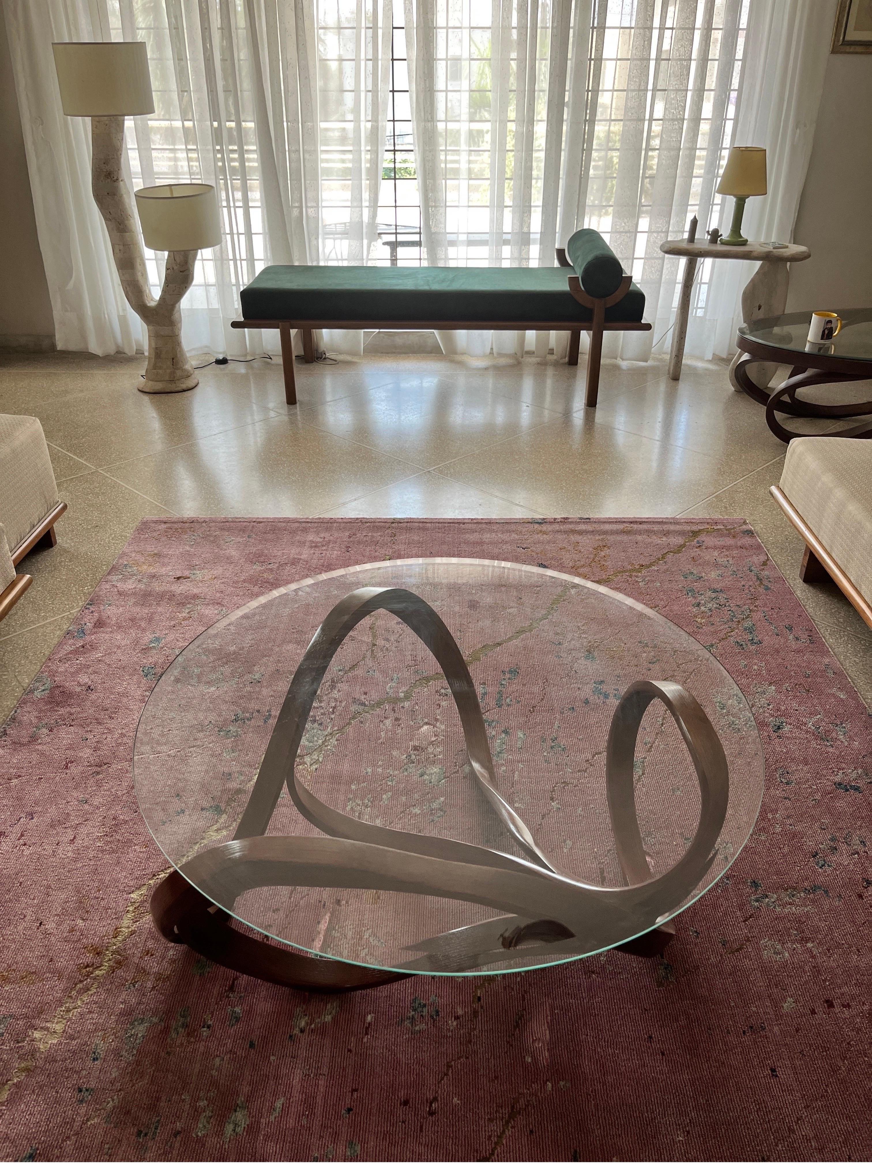 The center table has a free-form base to support the round glass top. The wood bends and curves with beautiful flows to create a design without a frame for the top. The handcrafted details on the piece such as the curves, varying thickness of the