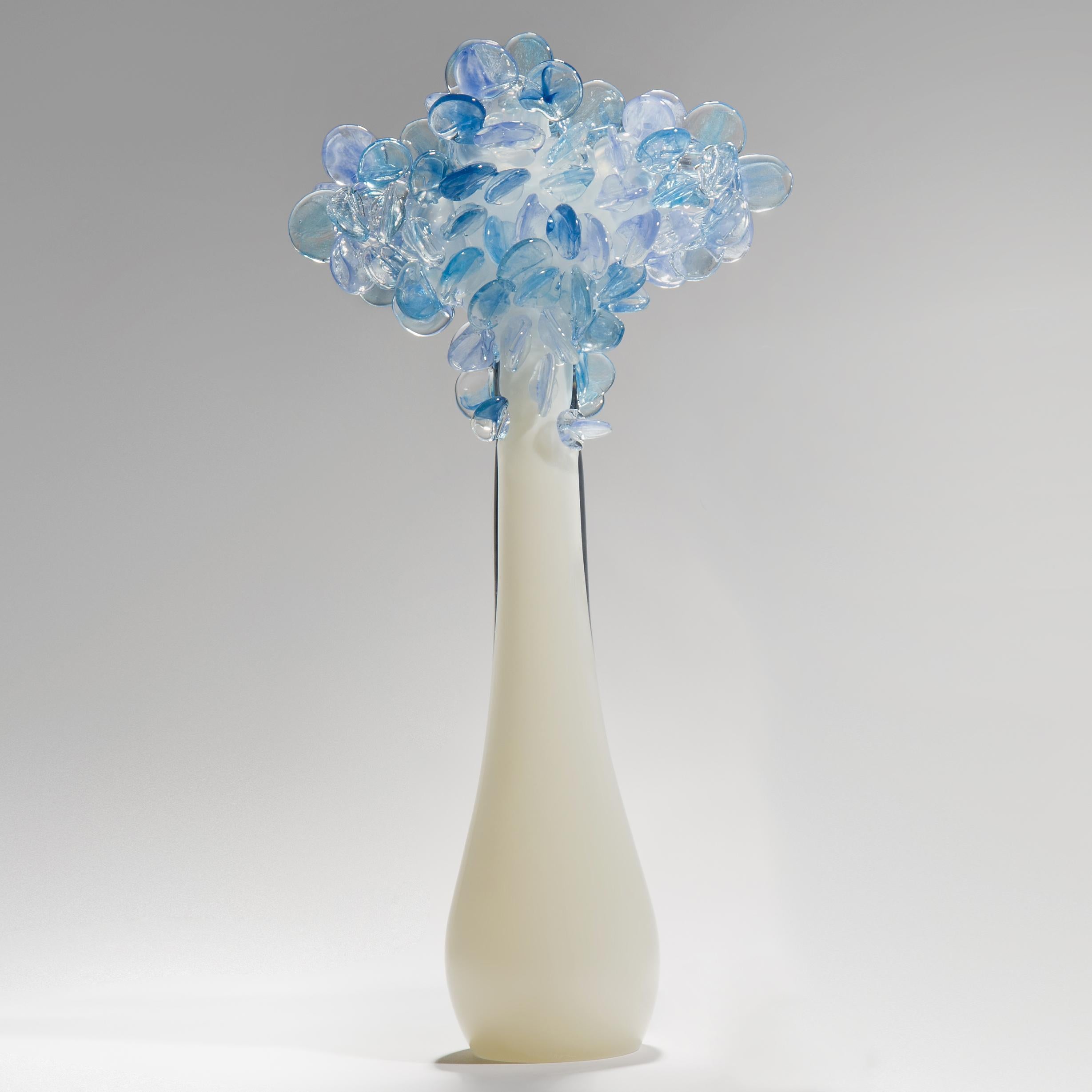 Enchanted dawn in tall blue, is a unique glass tree sculpture by the British artist Louis Thompson. The initial tree trunk form has been hand blown in clear and ivory/alabaster colored glass. The top has been covered in free-hand-sculpted leaves,