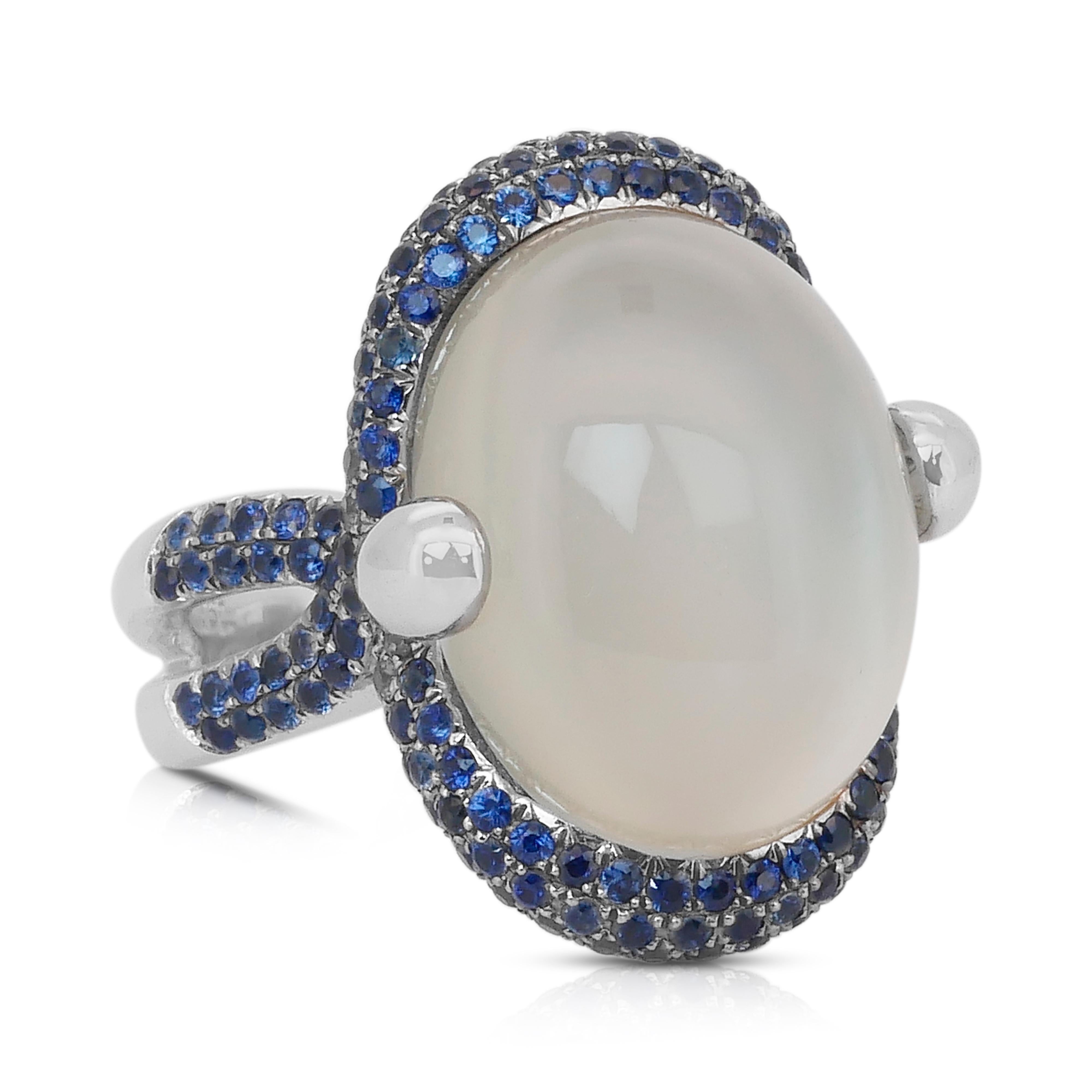 Whiting - Bague en or blanc 18 carats avec pierres de lune et saphirs - Certifiée IGI

Cette bague en or blanc 18 carats au charme céleste est ornée d'une captivante pierre de lune ovale de 8,00 carats, connue pour son éclat éthéré et son allure