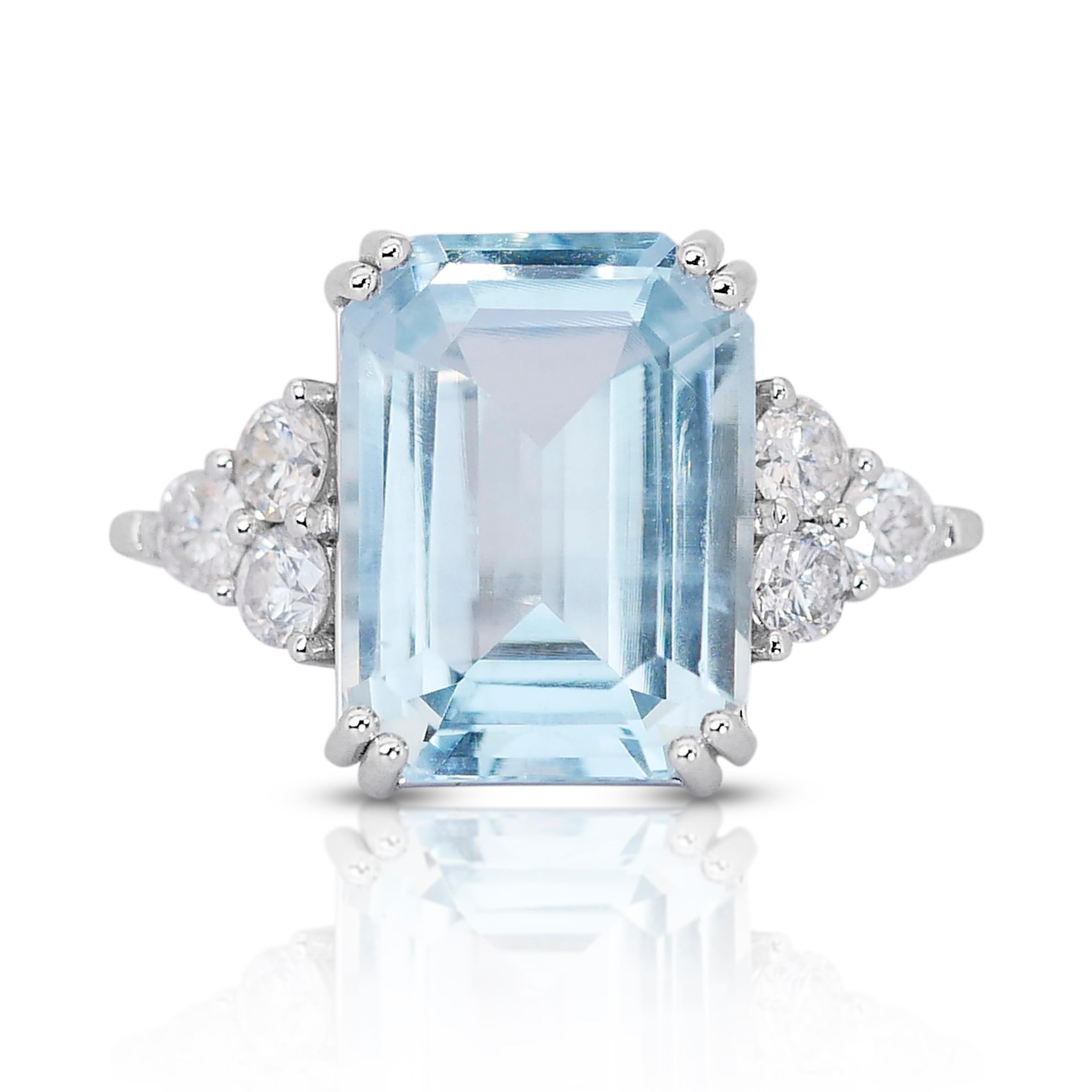 This enchanting ring features a striking emerald-cut aquamarine as its centerpiece, boasting a generous weight of 8.80 carats. The aquamarine displays a serene light or pale blue hue, reminiscent of a tranquil ocean on a sunny day. With its