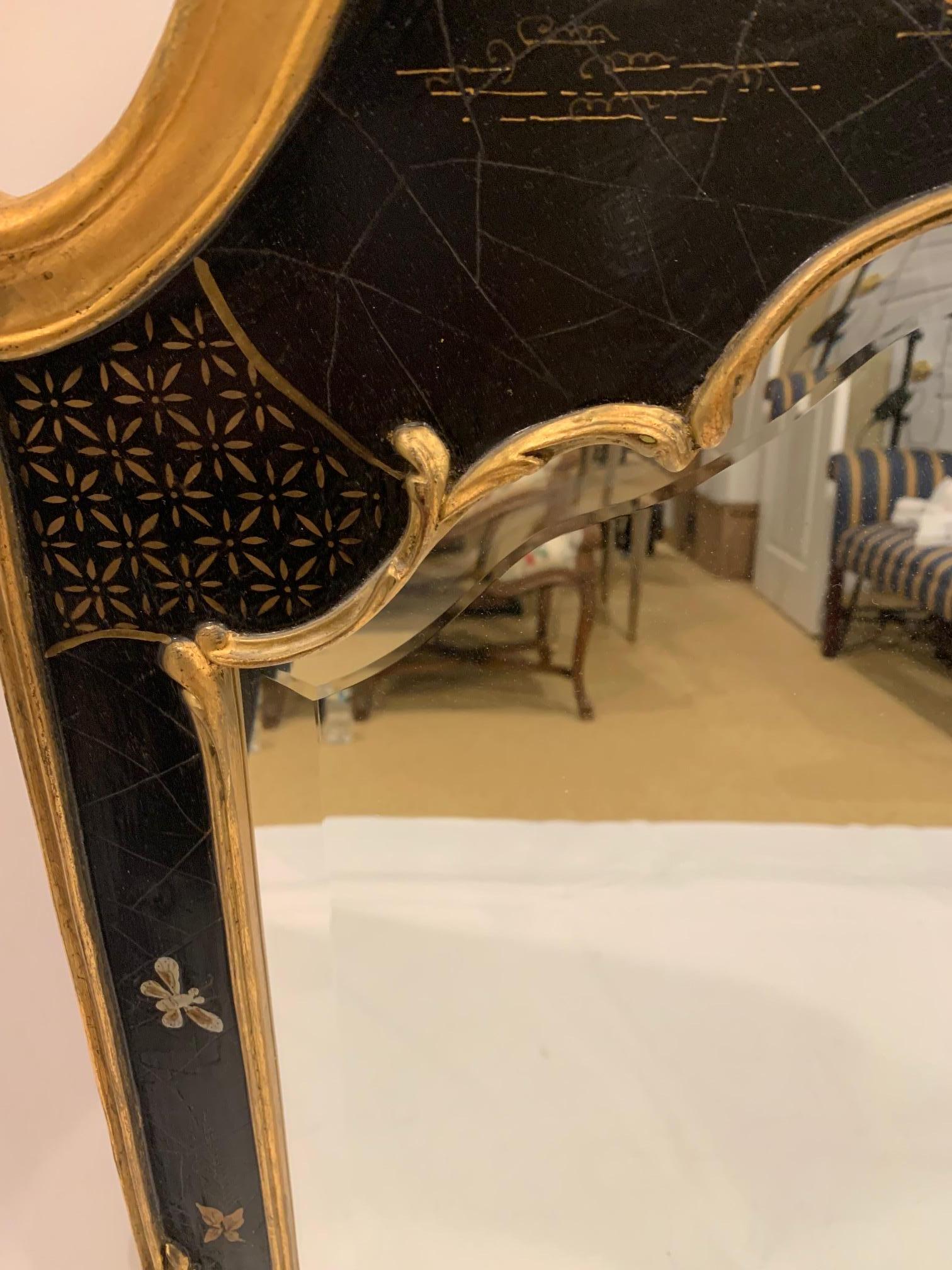 Strikingly elegant chinoiserie style wall mirror having gold leaf and hand painted frame. The black background offsets the figures and pagodas in primary colors of red, green and blue. The ornately gilded scalloped top is especially beautiful. And