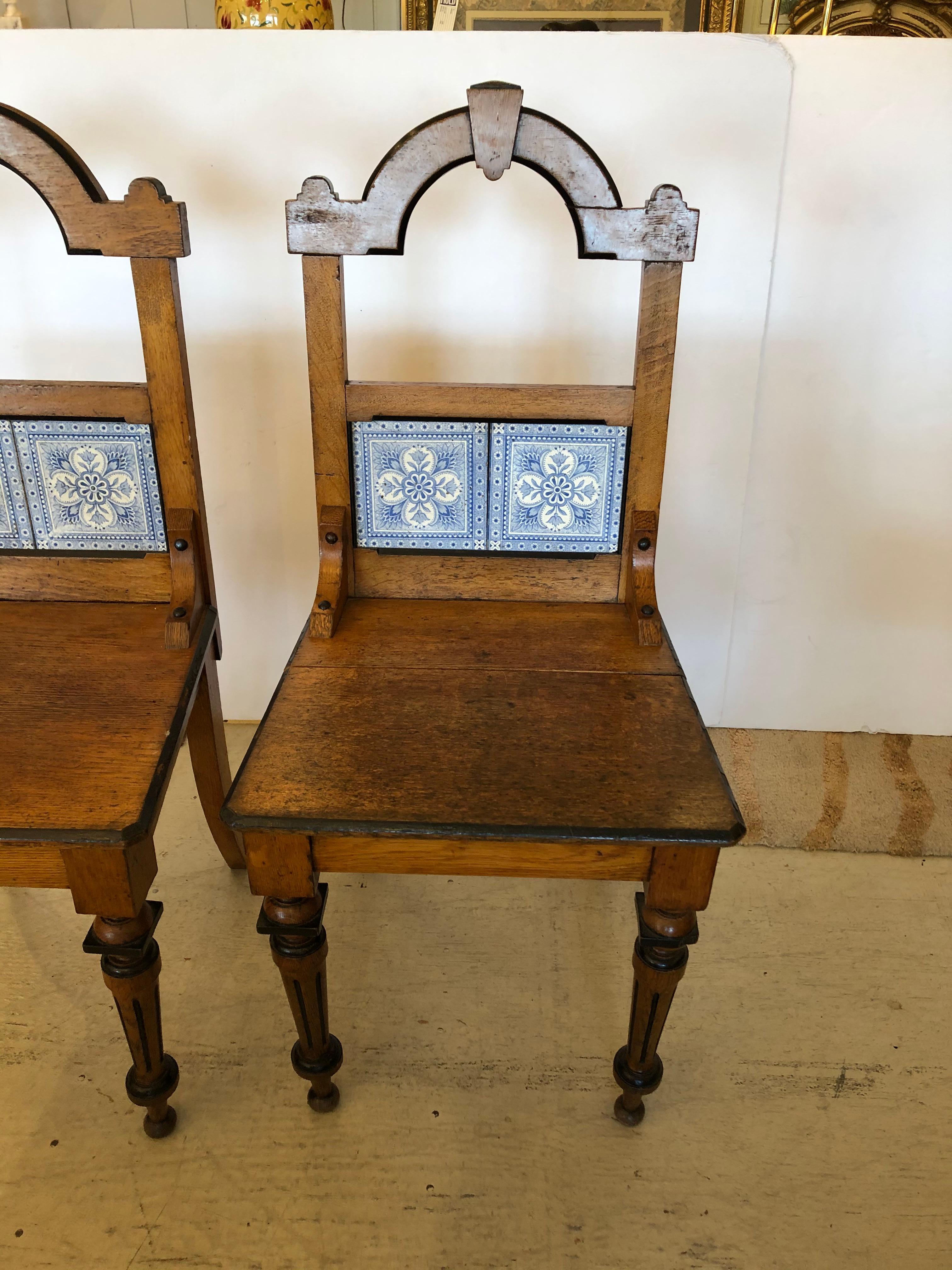 We've never seen a pair like these totally charming French honey oak upright side or hall chairs having arts and crafts style, blue and white Delft tile on the backs, and charming turned legs and scalloped tops. Sturdy and functional as extra