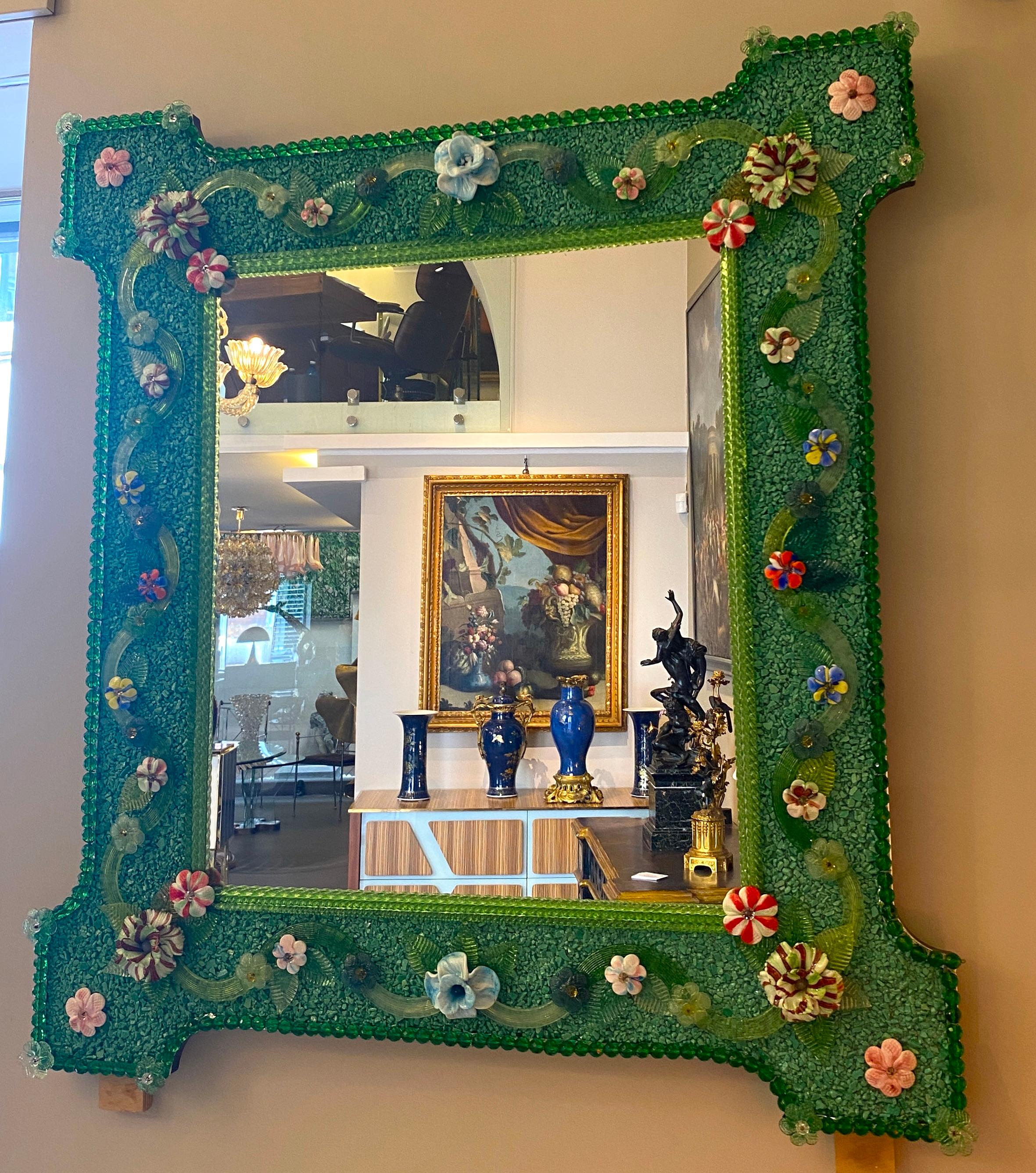 Charmant miroir vénitien avec cadre vert. Le long des bords du cadre se trouvent des accents de corde en verre vert et de nombreuses fleurs multicolores en verre pasta vitrea.
Exécuté par le grand maître de Murano.
Excellent état.
  