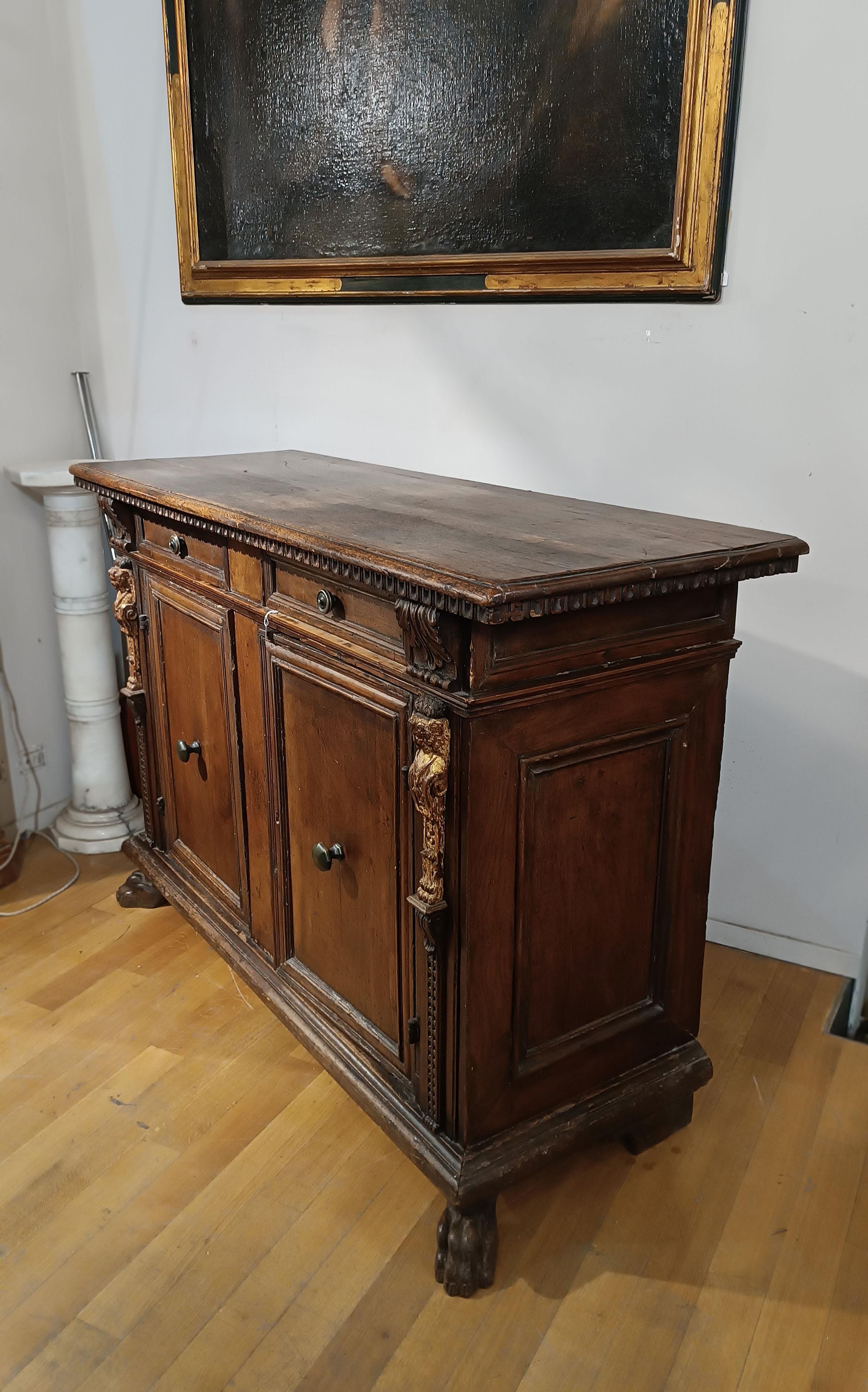 Splendid sideboard in solid walnut, finely carved with refined decorative details. The cabinet has two doors that open onto two large shelves, and two drawers on the front. The classical finishes include metope carvings under the top and capitals on