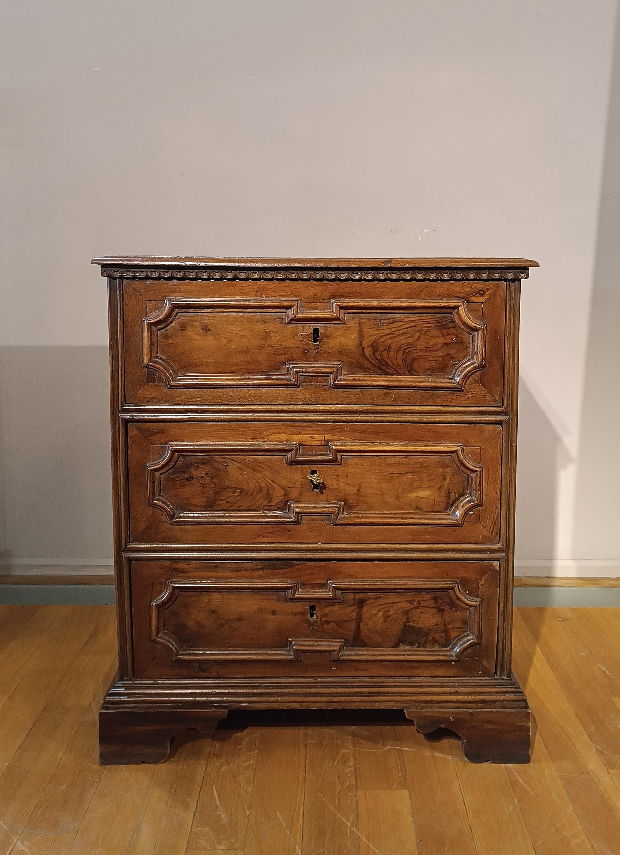 Elegant small chest of drawers in solid light walnut wood. The decorative details, such as the bracket feet and the solid wood frames carved with lozenges on the front and sides, give the furniture a timeless elegance. The three large drawers offer