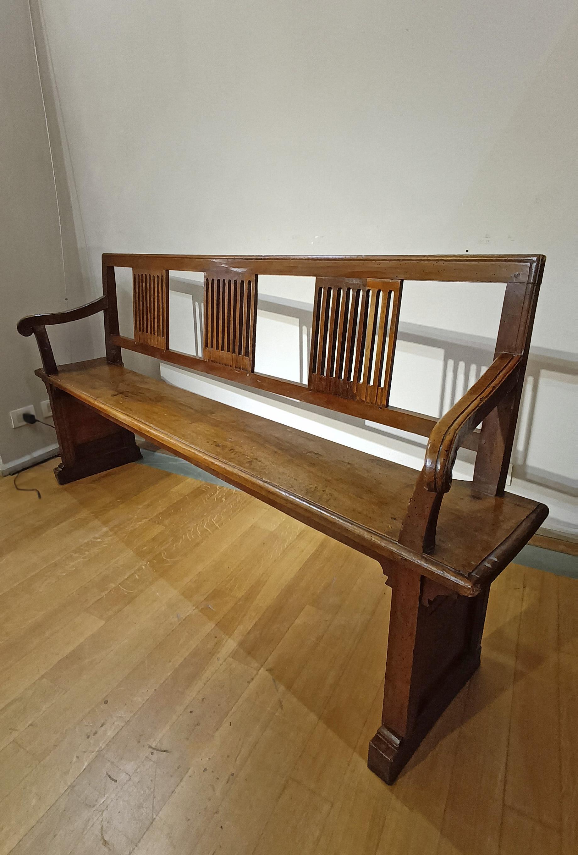 Splendid entrance bench in solid walnut, characterized by a carved backrest with linear decorations on three parts. The shoulder rest was also made from a single piece of fine walnut wood. The bench has two elegant armrests on the sides, slightly