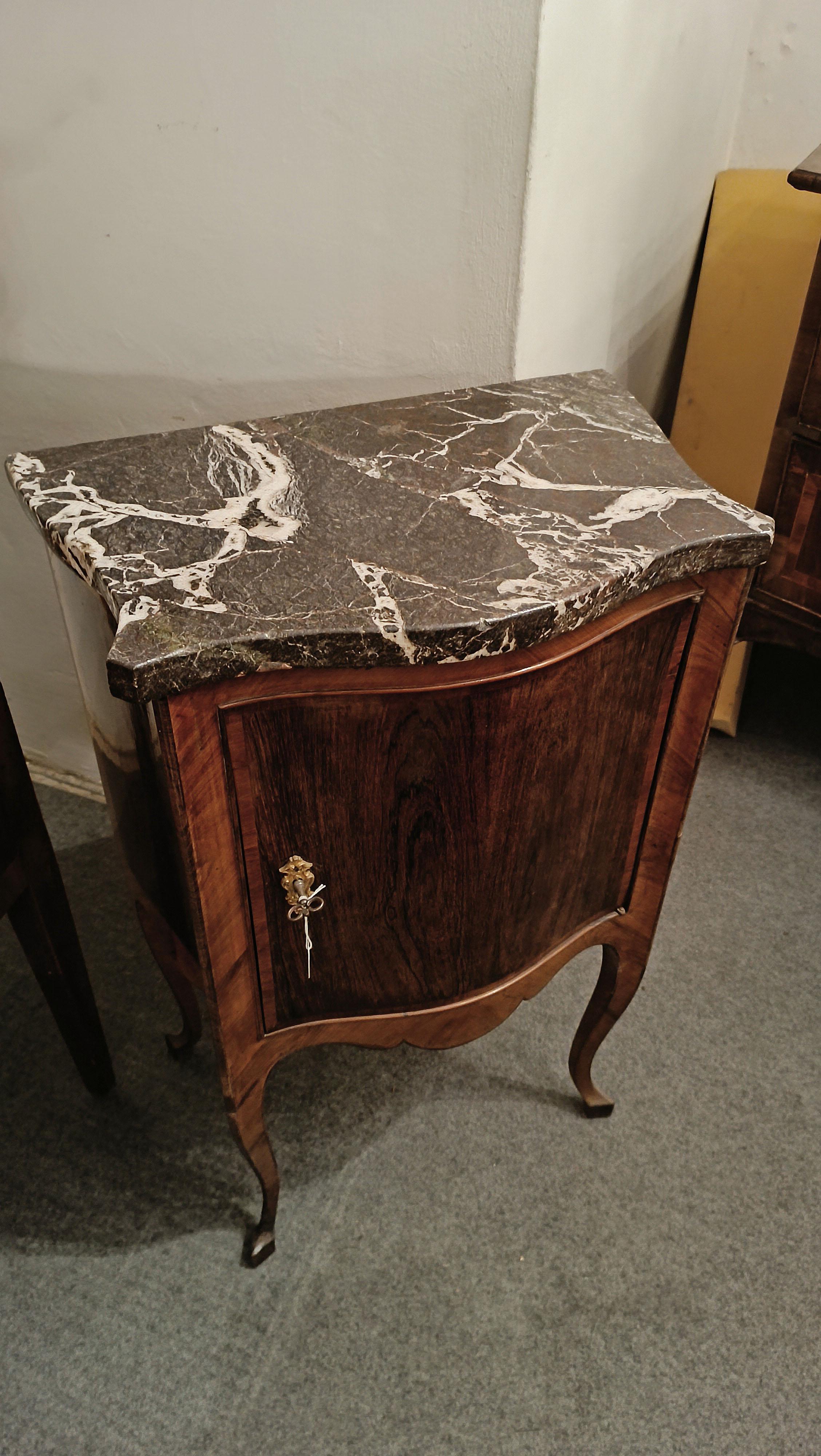 Elegant crossbow bedside table made of dark walnut, with a gray marble top with white and red streaks. The thin everted legs give lightness to the design, while the door, which can be opened with a key, offers a practical internal shelf for storing