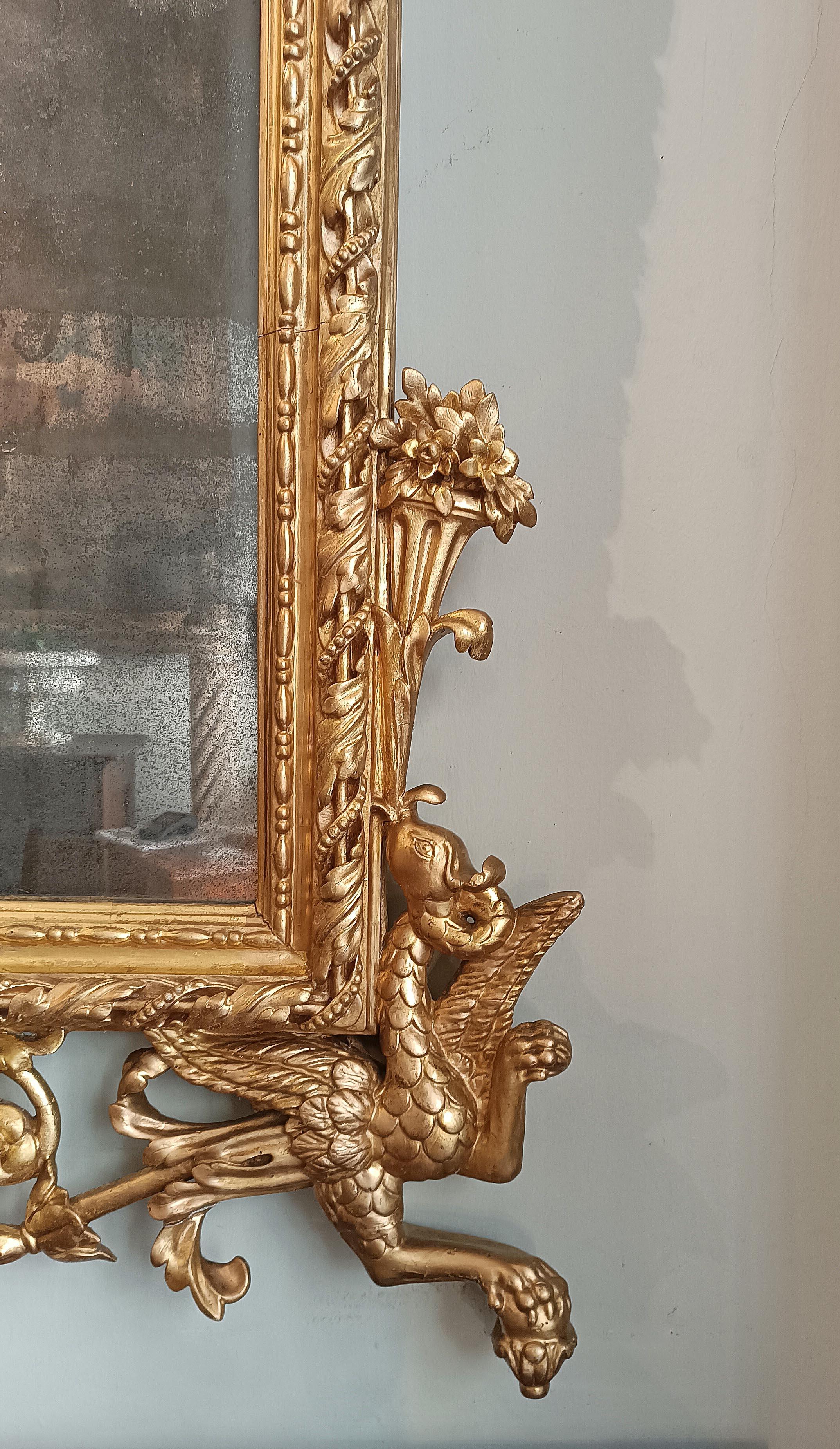 Beautiful neoclassical mirror with frame in carved pine wood and gilded with pure gold leaf. The frame is carved with vegetal spirals that run along the entire surface, of great refinement. Furthermore, the decorations in the lower part feature