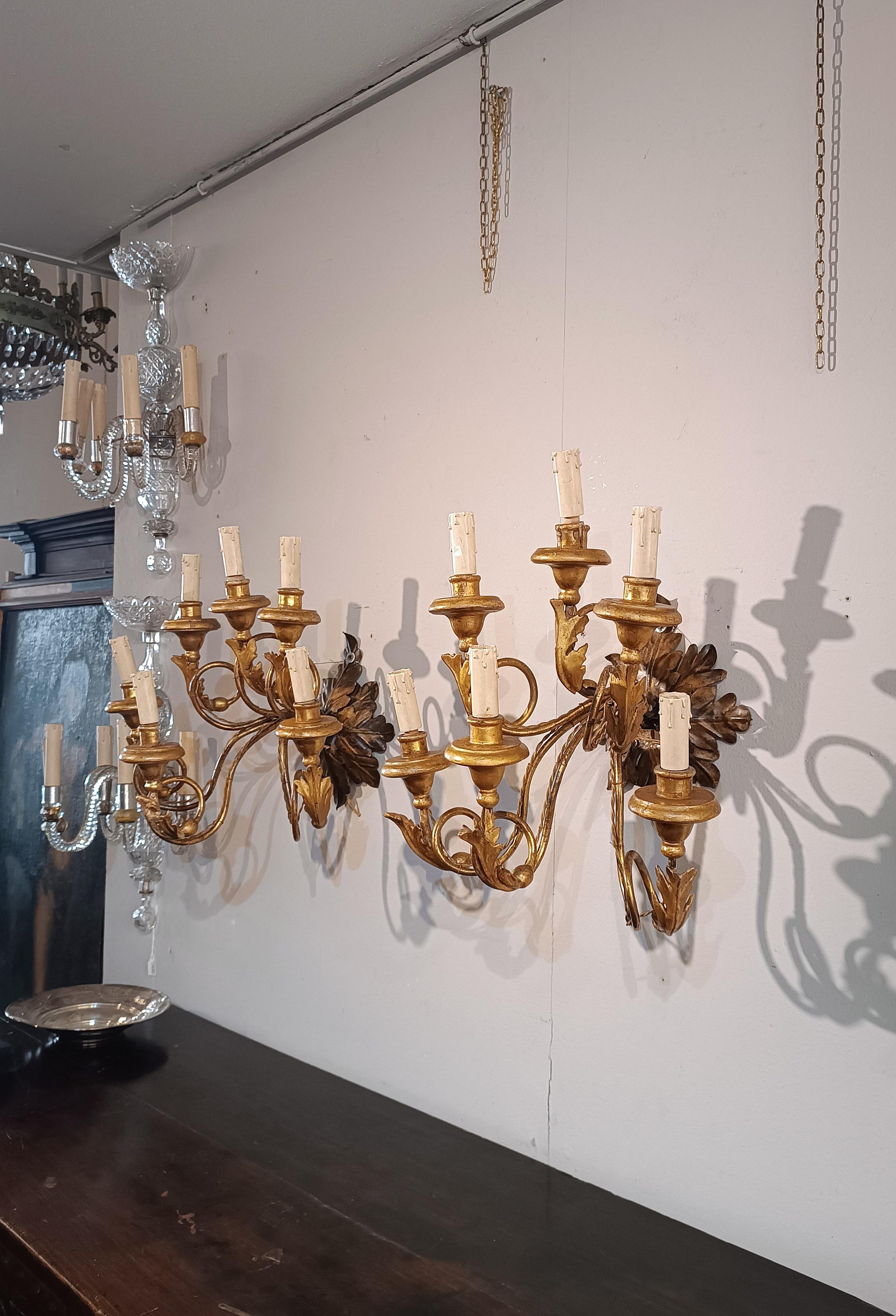 Espléndida pareja de apliques de 6 luces, de hierro dorado y madera tallada y dorada. Los apliques presentan un rosetón de hierro forjado forjado a mano, para fijar a la pared, que sostiene los brazos. Los rosetones y los brazos de los apliques