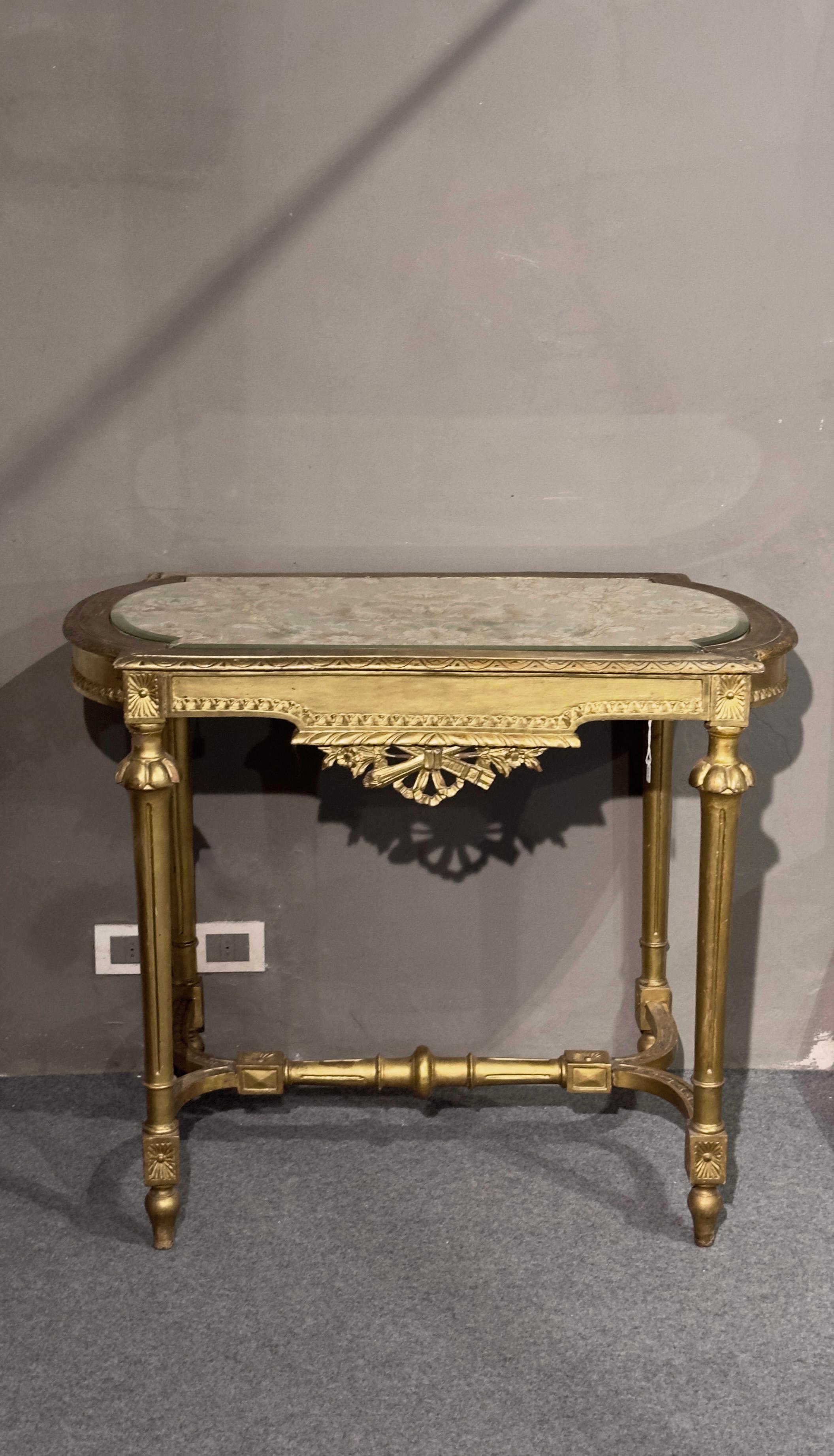 Splendid and elegant gilded wooden coffee table, in neoclassical style. The rectangular top with circular sides is enriched by a refined fabric covered by glass, which gives further charm to the piece of furniture. The decorations, inspired by the
