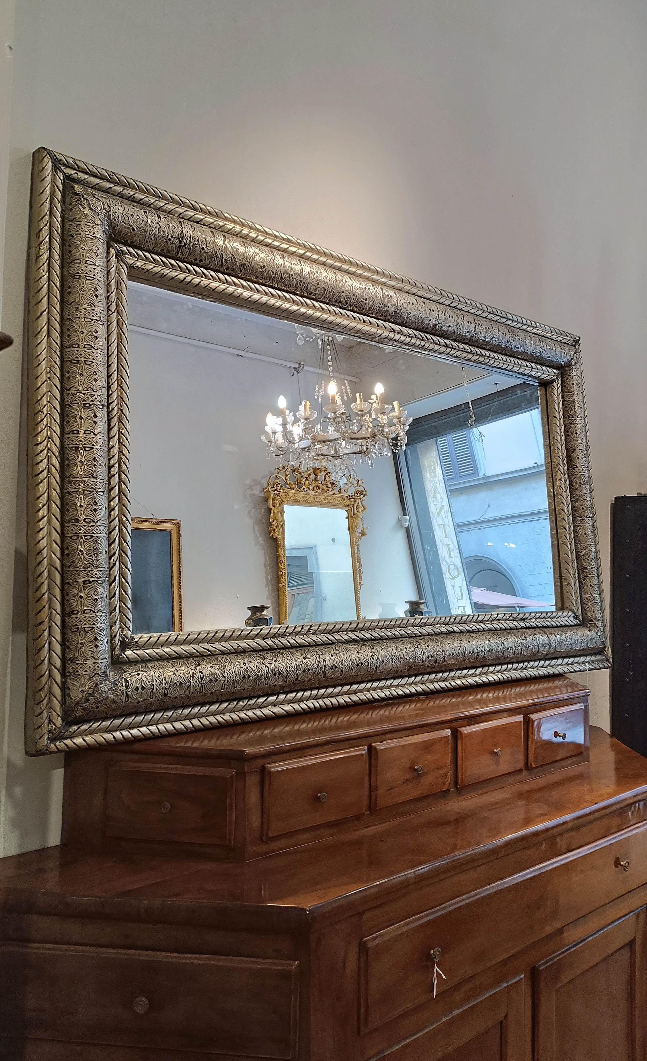 Beautiful and elegant large mirror in silvered copper foil, beaten and engraved by hand and applied on carved wood. The frame has a complex decoration, divided into three parts: two elegant weaves that frame a convex central plate engraved with