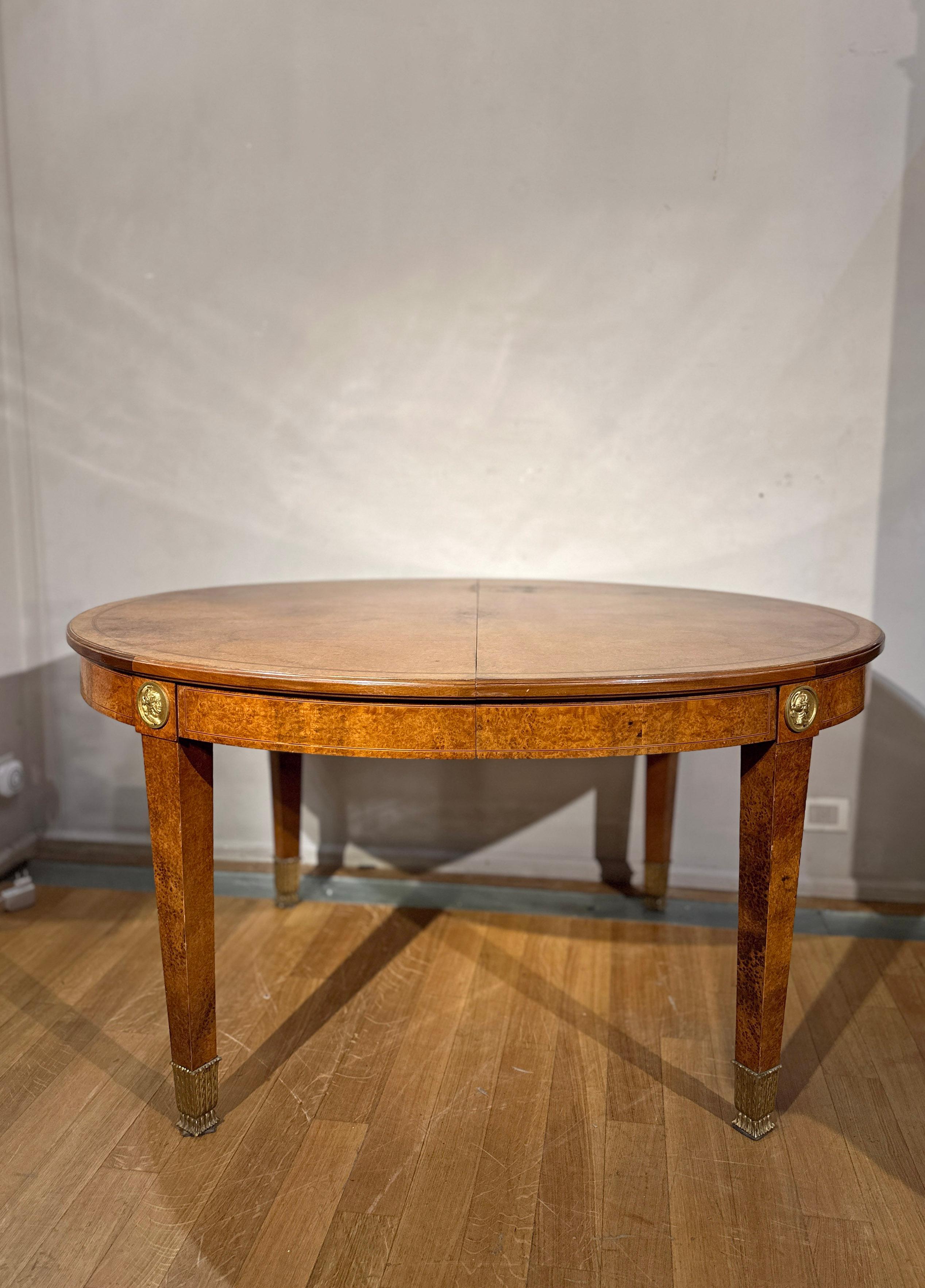 Splendid oval table in maple wood with gilt bronze finishes. The medallion finishes on the lower band depict characters from ancient iconography, while the leaf shoes on the four truncated pyramid legs add a touch of elegance. The table can be