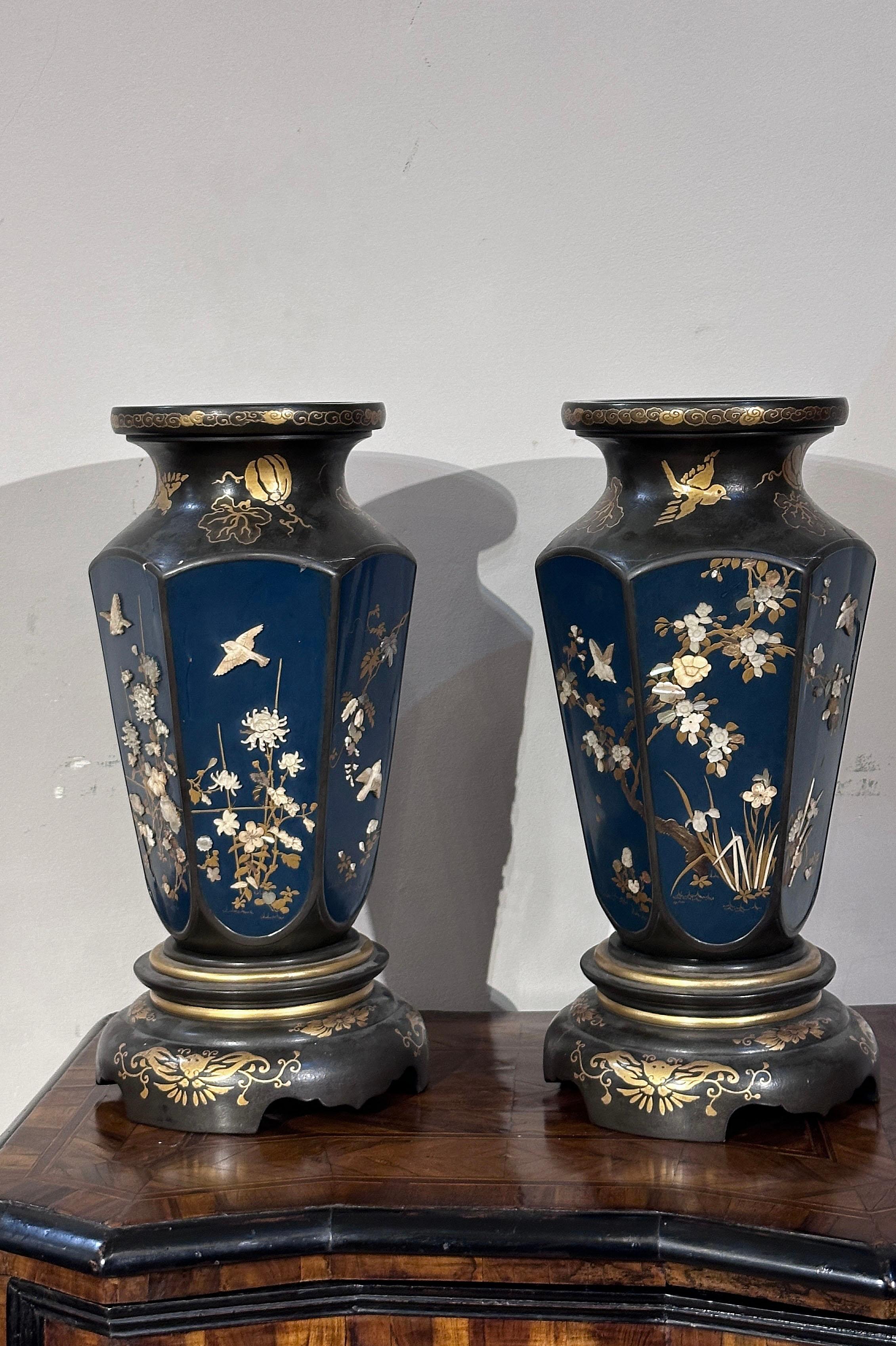 Beautiful pair of wooden vases lacquered in an elegant shade of blue, and decorated with light wood inlays and golden finishes. The inlays depict delicate floral and bird motifs, creating an idyllic and evocative atmosphere. The golden finishes,