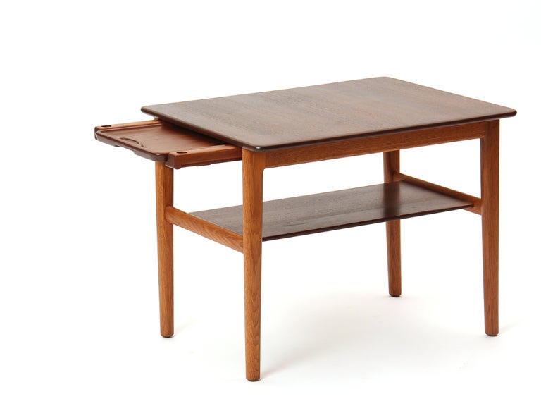 A two-tier Scandinavian Modern end table designed by Hans Wegner with a solid teak top. 
Table features built-in shelf and pullout serving tray on oak legs. Crafted by Johannes Hansen in Denmark circa 1960s. Branded with 'Johannes Hansen,