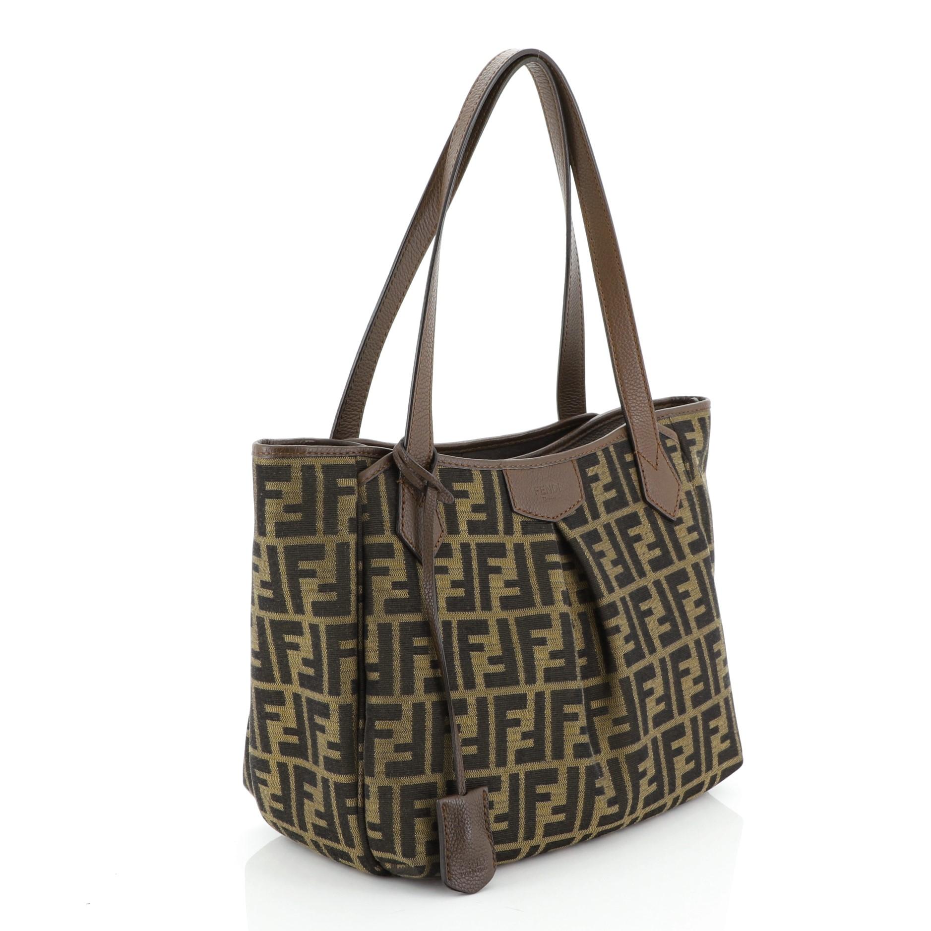 This Fendi Shopping Tote Zucca Canvas Medium, crafted in brown zucca canvas, features dual handles, leather trim, and gold-tone hardware. Its zip closure opens to a brown striped fabric interior with slip pockets. 

Estimated Retail Price: