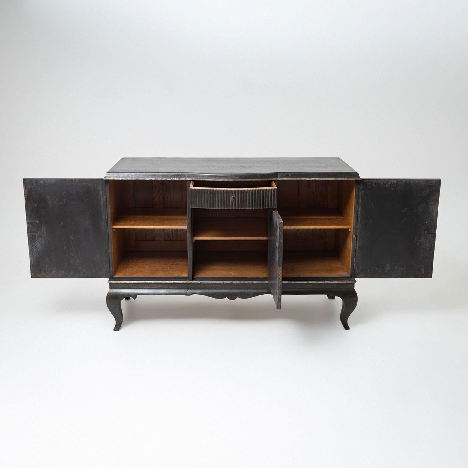 An elegant sideboard from the 1930s, featuring an anthracite finish. The front is adorned with silver-patinated oval frames and decorative elements, adding a distinctive touch to the piece. The sideboard includes three doors and a central drawer,