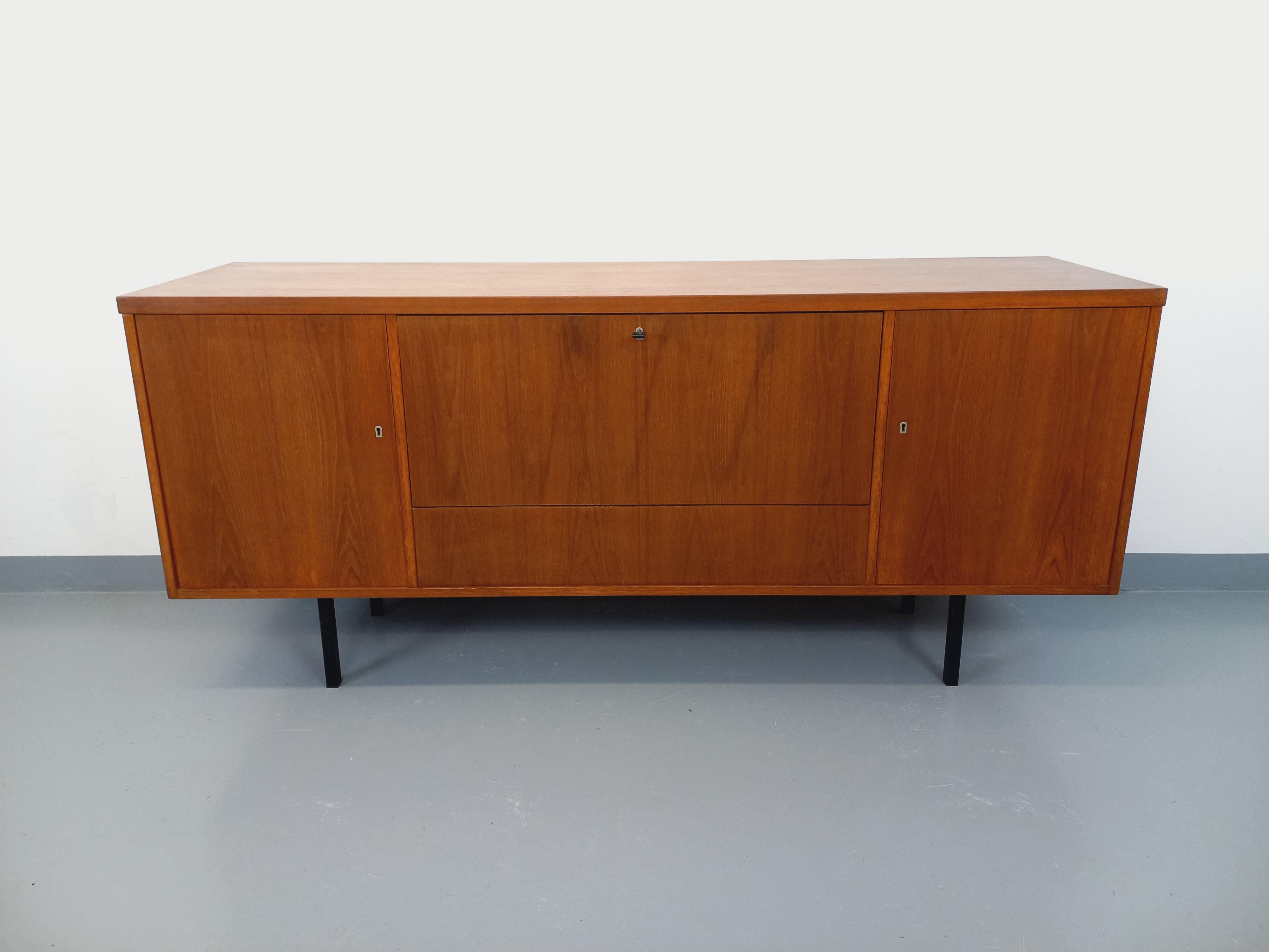 Enfilade in stile scandinavo vintage degli anni 60-70, in teck, piedini in métal noir. 1 porta con parte di bar e 2 porte con ripiani, una clé per le 3 serrures. Très bon état général avec quelques signes du temps qui passe. Può essere utilizzato al
