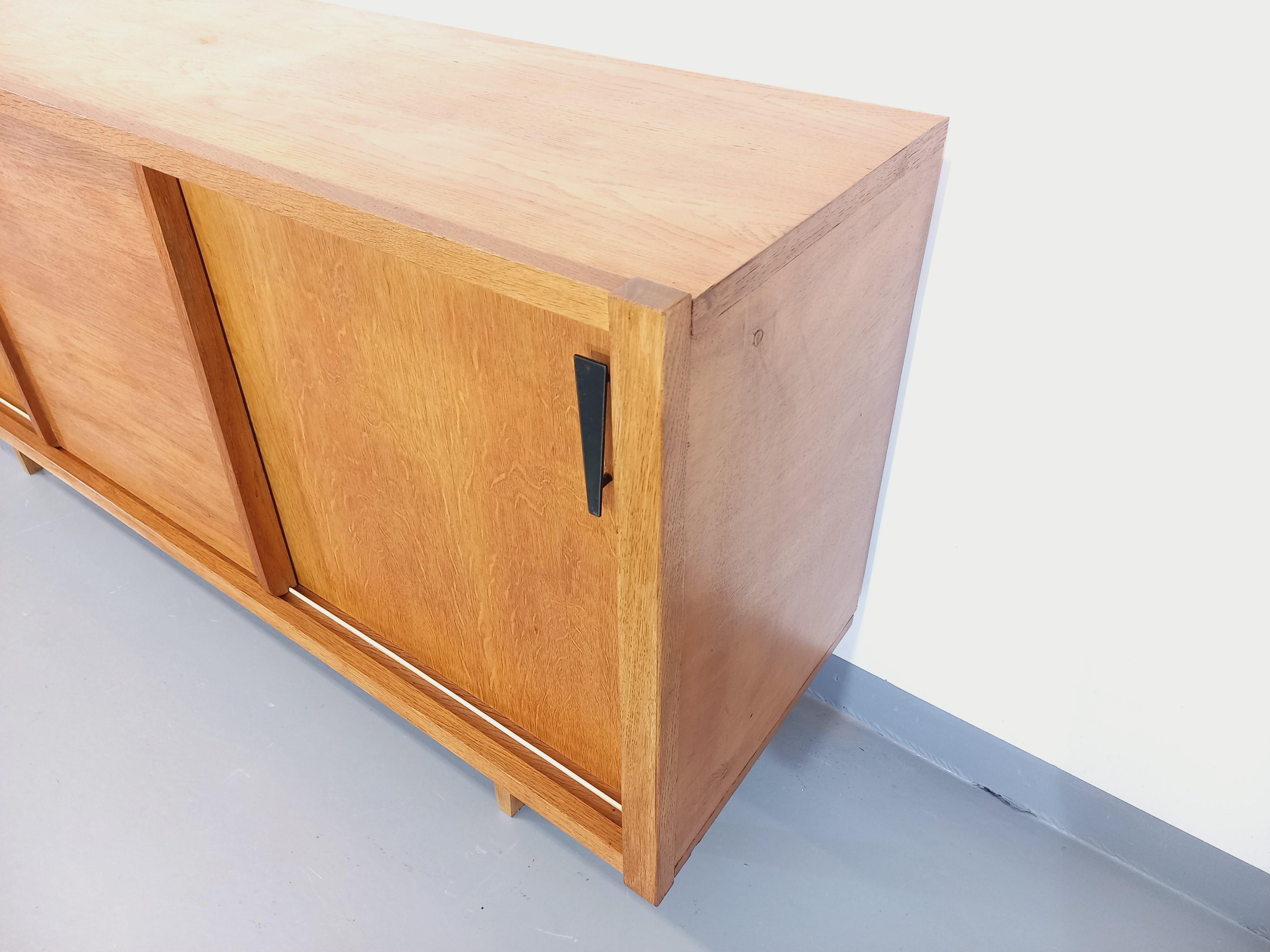 Enfilade vintage des années 60, en bois de chêne blond doré, très beau design moderniste avec poignées asymétriques en métal noir et pieds compas. Beaucoup de rangements : 3 coulissante Ports mit verschiedenen Etagen und Innenschränken. Sehr guter