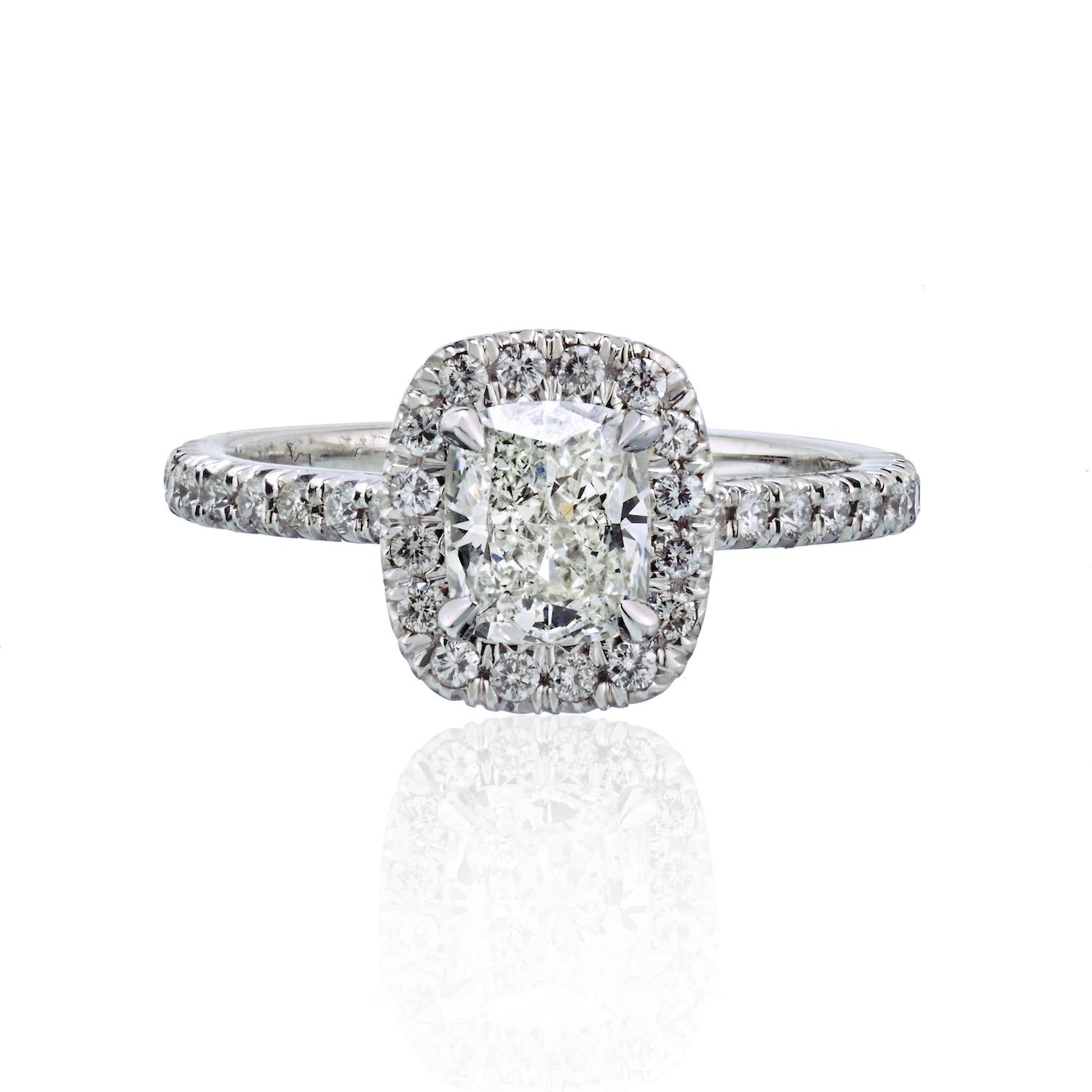 This lovely cushion cut halo set diamond engagement ring features a 1.06-carat center diamond in a sparkly round brilliant diamond setting. Round cuts set around the center stone and along the ring's shank. Four prongs securely hold the center
