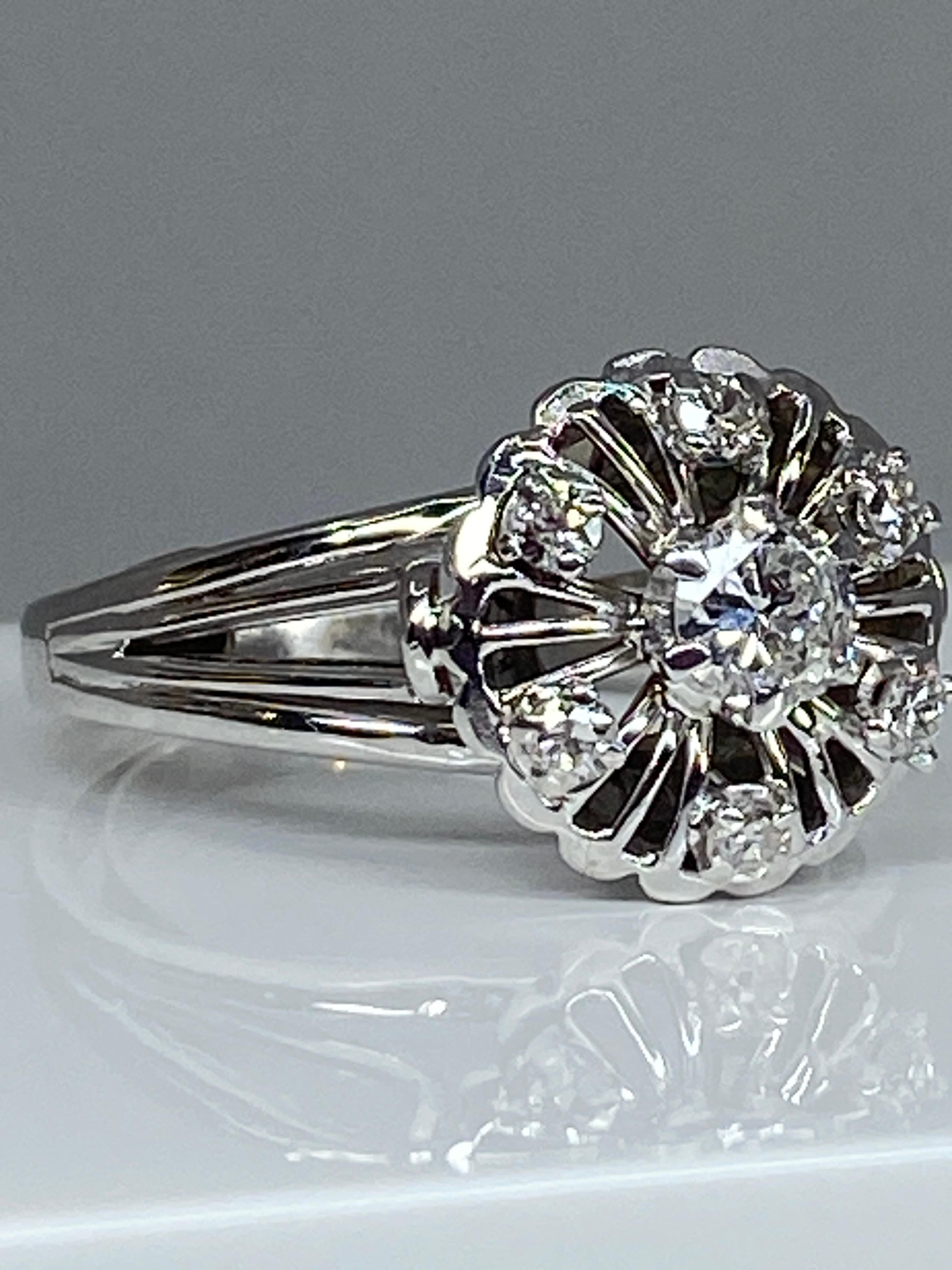 Ravissante bague de fiançailles en or 18 carats de forme fleur stylisée , ornée au centre d’un diamant de taille brillant pesant 0.25 carat environ, entouré de 6 diamants de taille brillant pesant 0.20 carat environ. L’ensemble est en serti griffes.