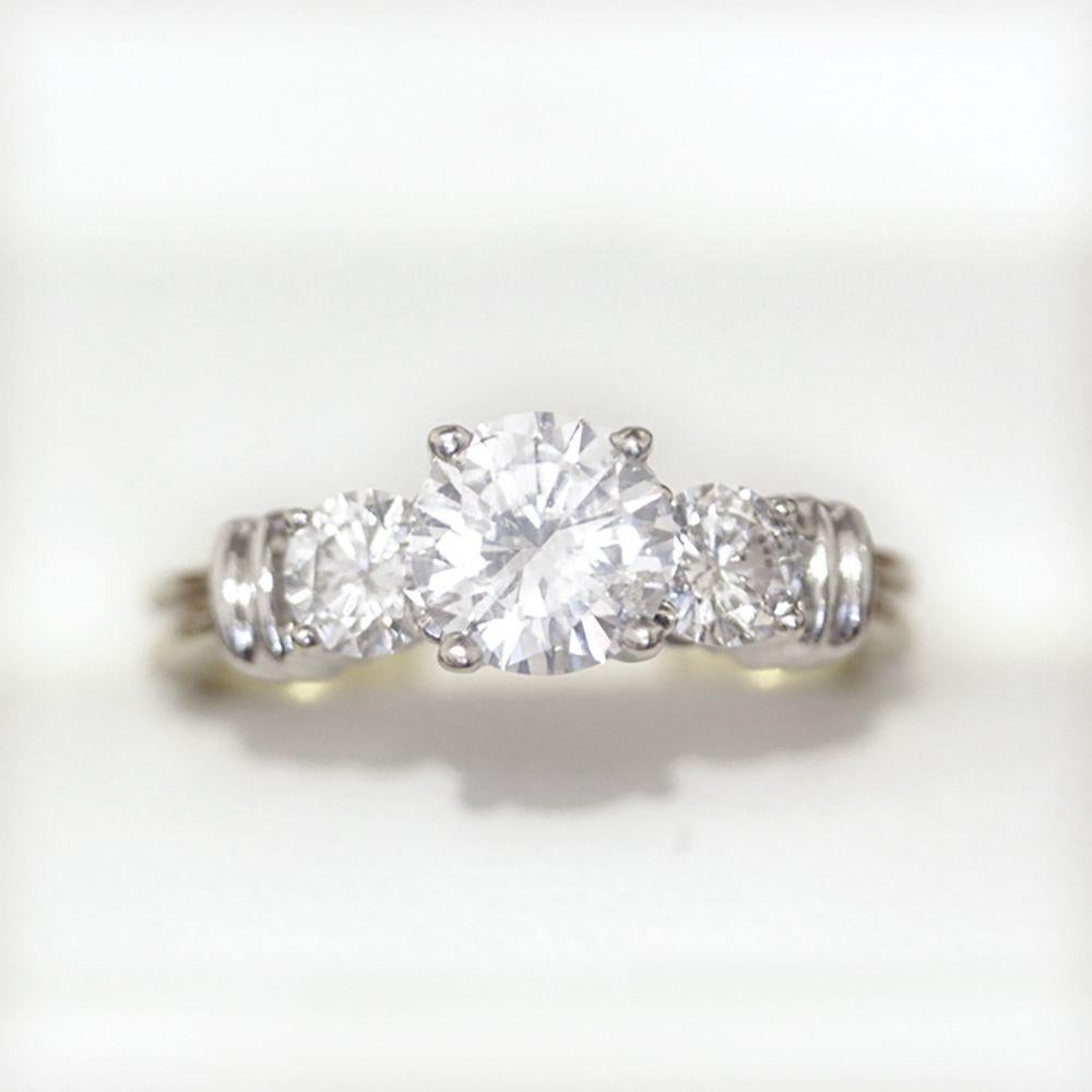 Mit 3 runden Diamanten im Brillantschliff aus Weißgold in 4-Krallen-Fassung mit gerillten Weißgold-Bügelschultern auf einem gerillten 2,6-mm-Gelbgoldband.

Diamanten 1 @ 6.76 x 3.82mm = 1.06cts H/I 

2 @ 4,3 - 4,25mm = 0,60cts G

Gesamtgewicht des