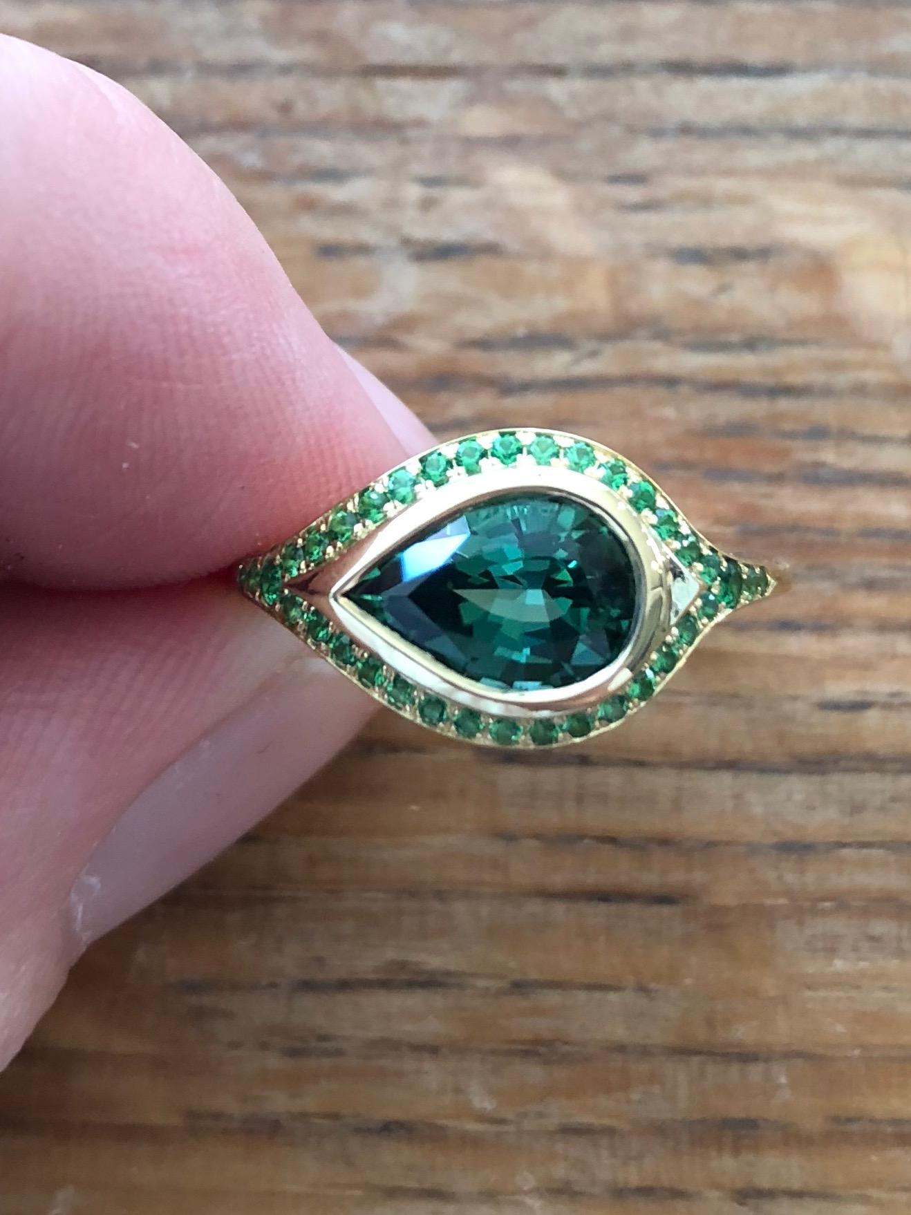An exceptional blue green tourmaline 2.46 ct (10.6x 7.3 x5.5mm) mine to market from Namibia, encircled with the finest tsavorites creates a ring absolutely luminous with color. One of a kind. A combination of old world techniques that only a hand