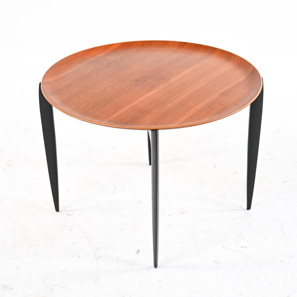 Practical and elegant, this side table consists of a removable circular tray top in teak veneer, perched upon an ebonized wood base that cleverly collapses for easy storage. Designed by Svend Willumsen and Hans Engholm for Fritz Hansen, produced in