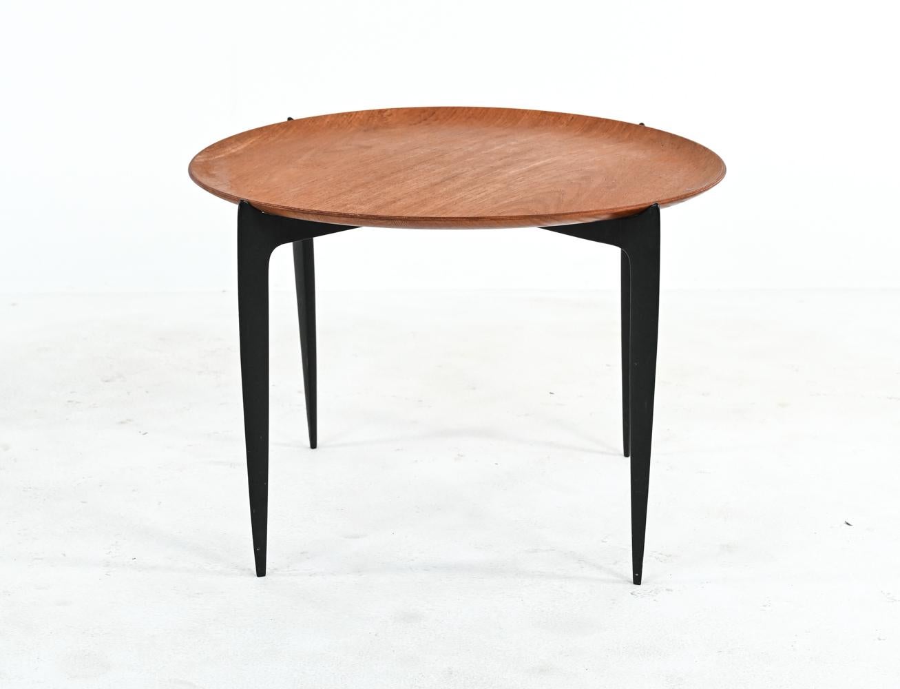 Practical and elegant, this side table consists of a removable circular tray top in teak veneer, perched upon an ebonized wood base that cleverly collapses for easy storage. Designed by Svend Willumsen and Hans Engholm for Fritz Hansen, produced in