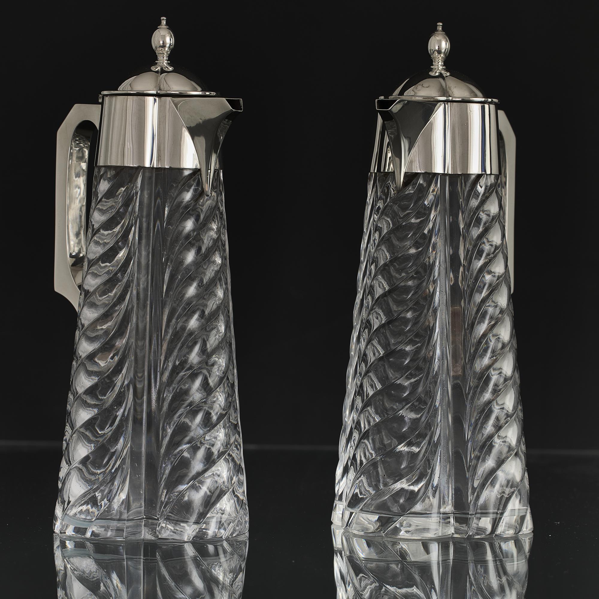 Pair of fine quality late-Victorian antique wine jugs with hand-blown quadra-form glass bodies deeply cut with swirling fluted decoration. The jugs are of a rare design that is both elegant and functional with each holding a bottle of wine. Each jug