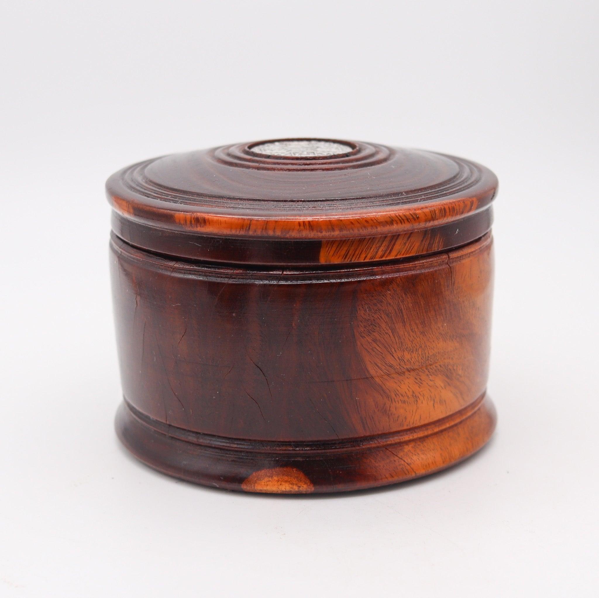 A George III tobacco round desk box made in England.

This is a beautiful round desk box created in England during the period of king George III, back in 1787. The box was finely carved in mahogany wood and embellished on top with a genuine silver