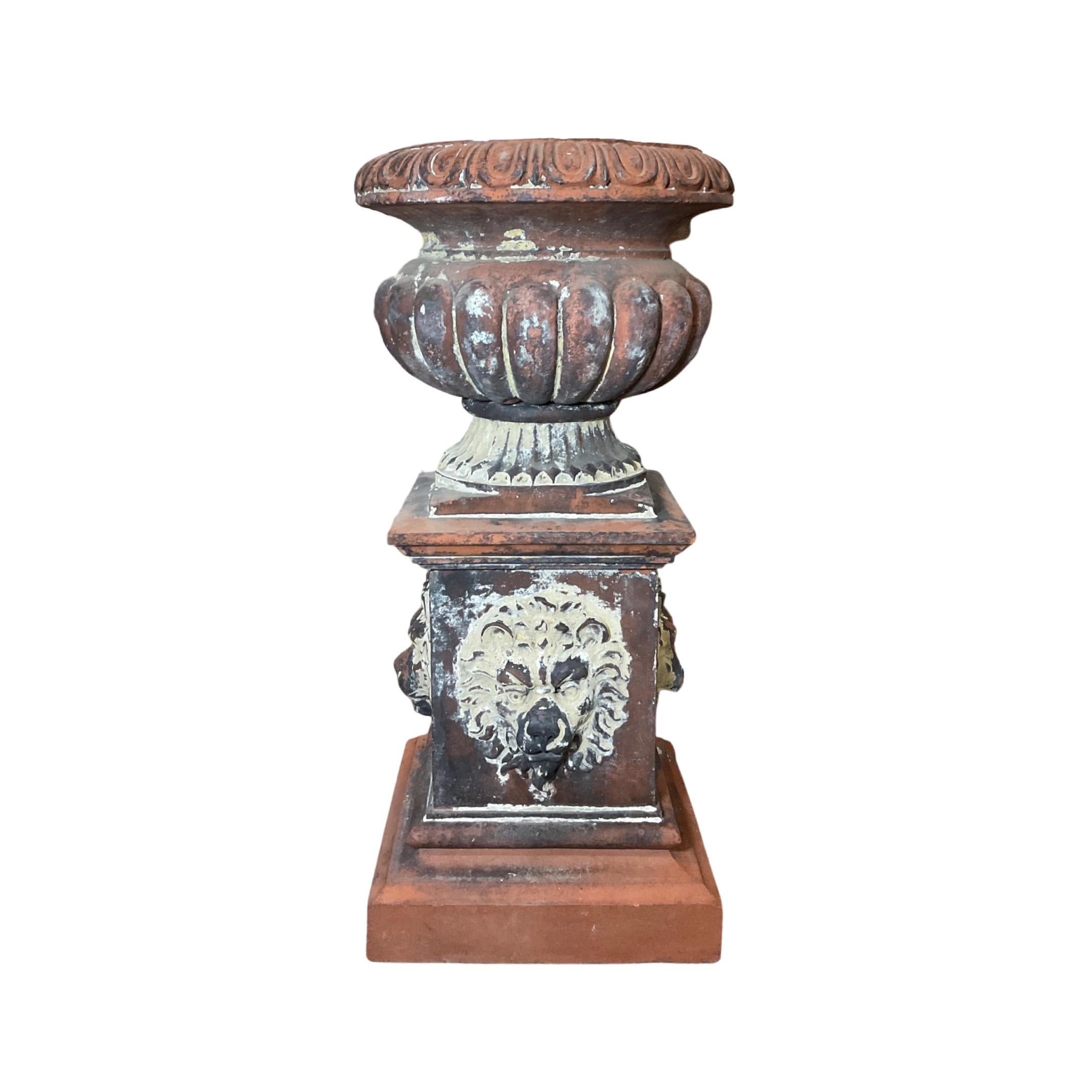 This England Terracotta Planter is an elegant 19th-century piece, crafted from durable terracotta and featuring intricate lion head motif carvings along the base. The planter comes with the base included, adding to its versatility when decorating