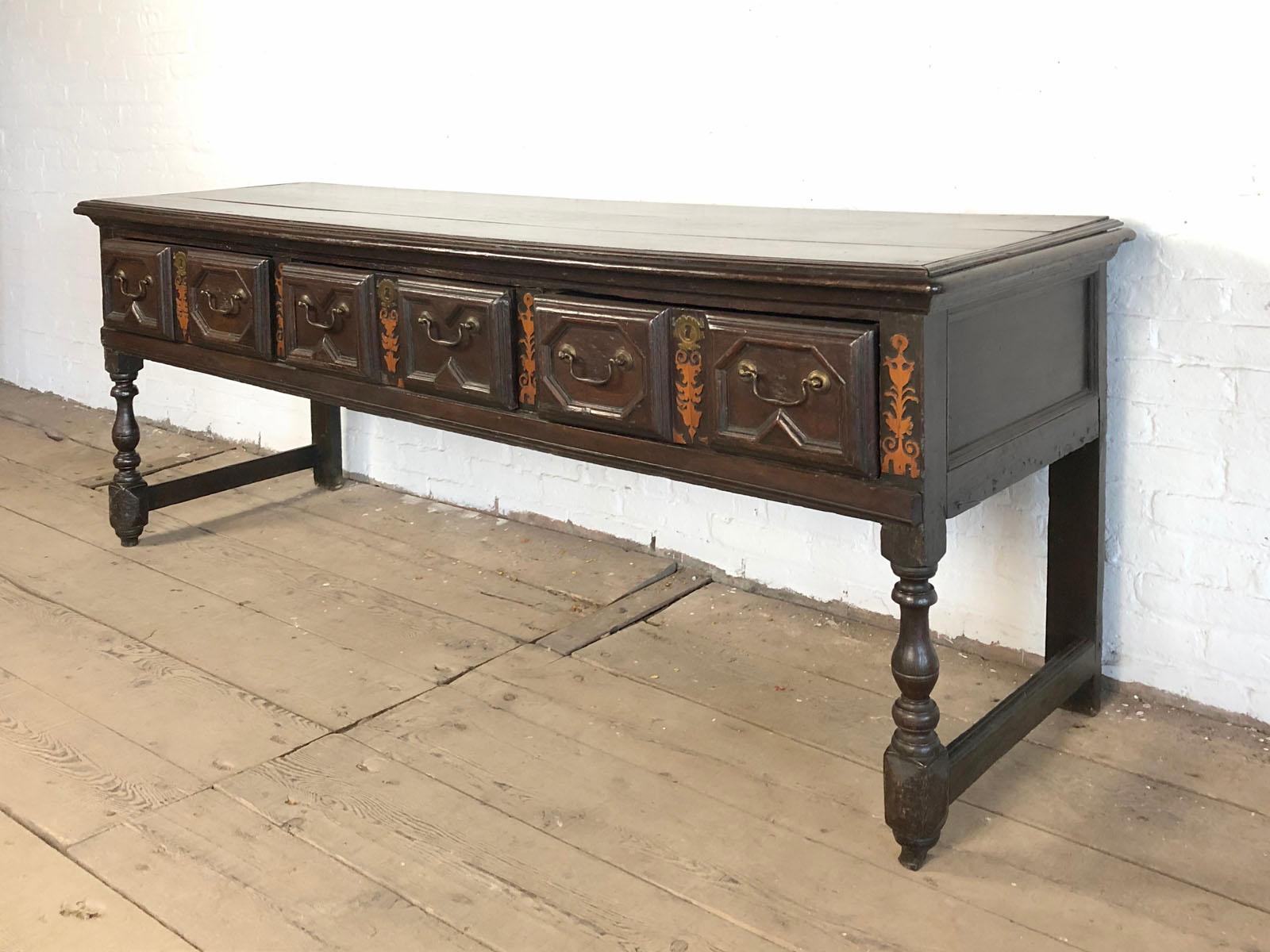 English oak 17th century open base long dresser, with a three-board top surrounded by a molded edge, above a frieze, containing three drawers, the drawer fronts with applied geometric moldings and decorated with bright stained fruitwood fretwork