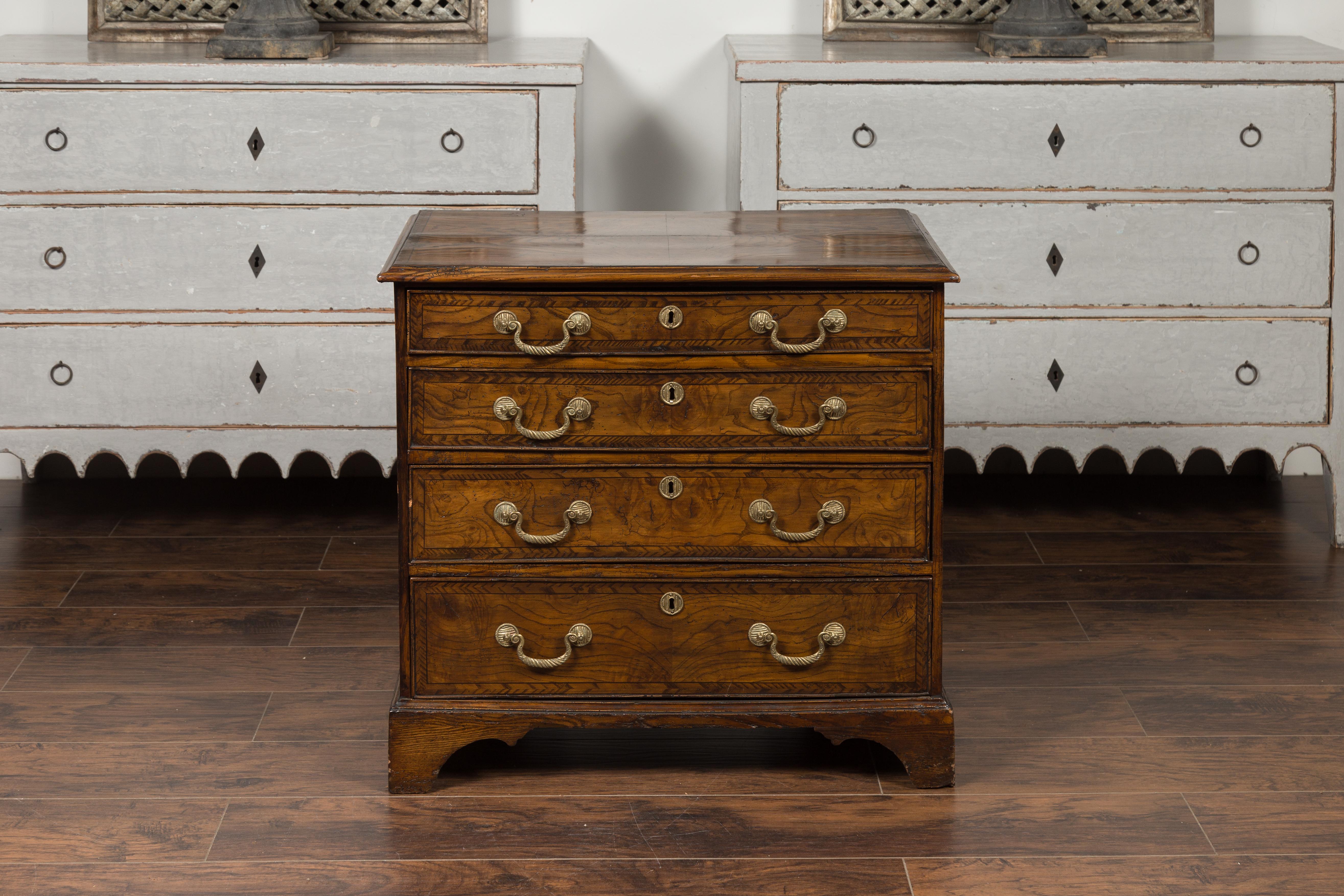 An English George III period burl wood chest-of-drawers from the early 19th century, with feather banding inlay and bronze inlay. Crafted in England during the reign of King George III, this burl wood chest features a rectangular top, sitting above