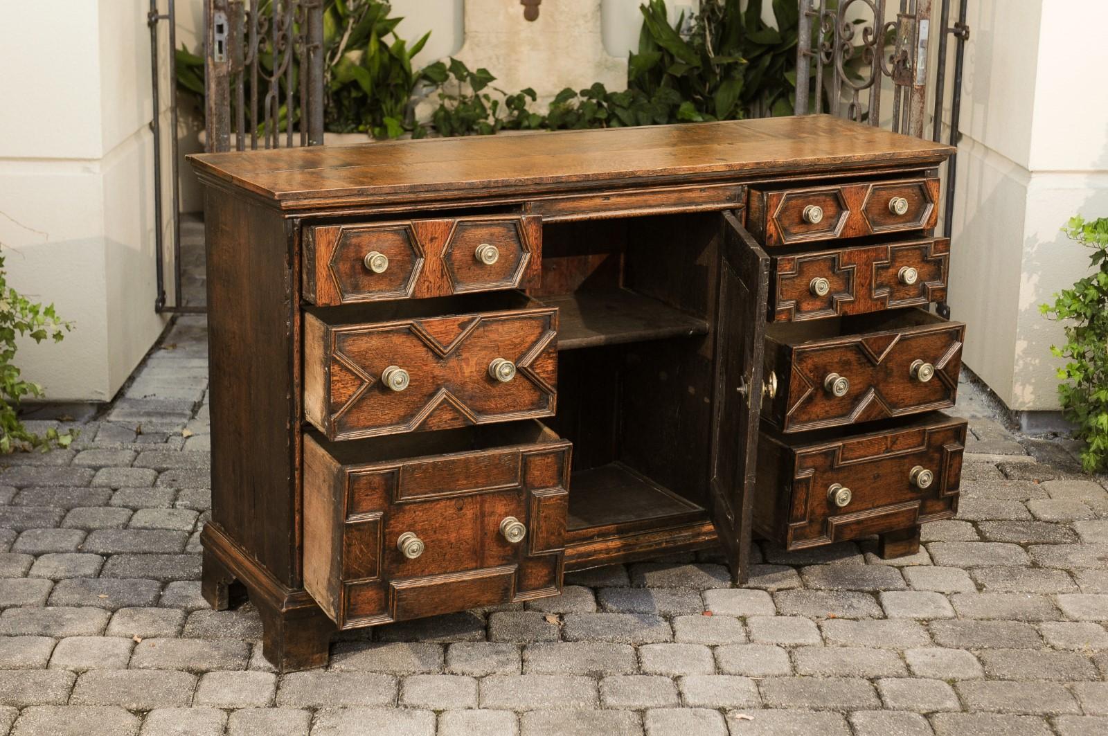 An English Georgian period geometric front oak buffet from the early 19th century, with single door and seven drawers. Born in England during the reign of King George III, this exquisite oak buffet features a rectangular planked top sitting above a