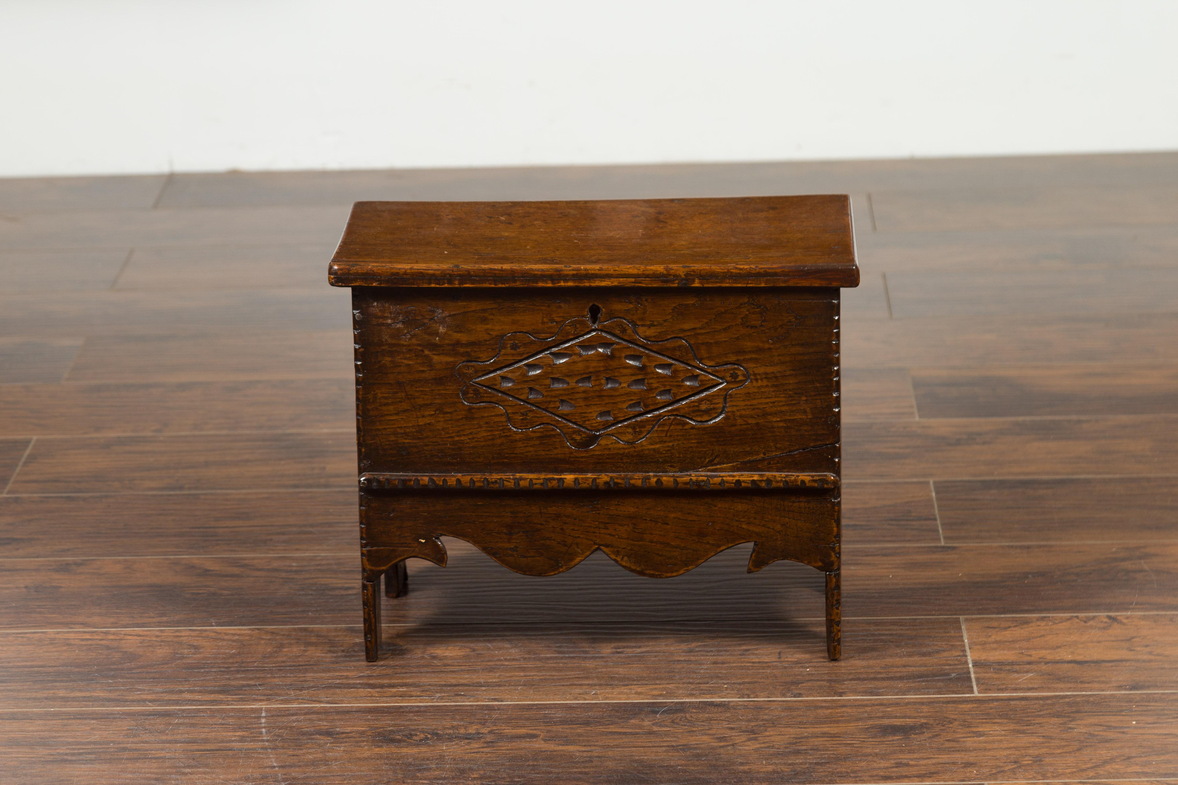 An English Georgian period mini oak coffer from the early 19th century, with carved motifs and scalloped apron. Born in England during the reign of King George III, this mini coffer features a lift top revealing a small storage area, resting upon a