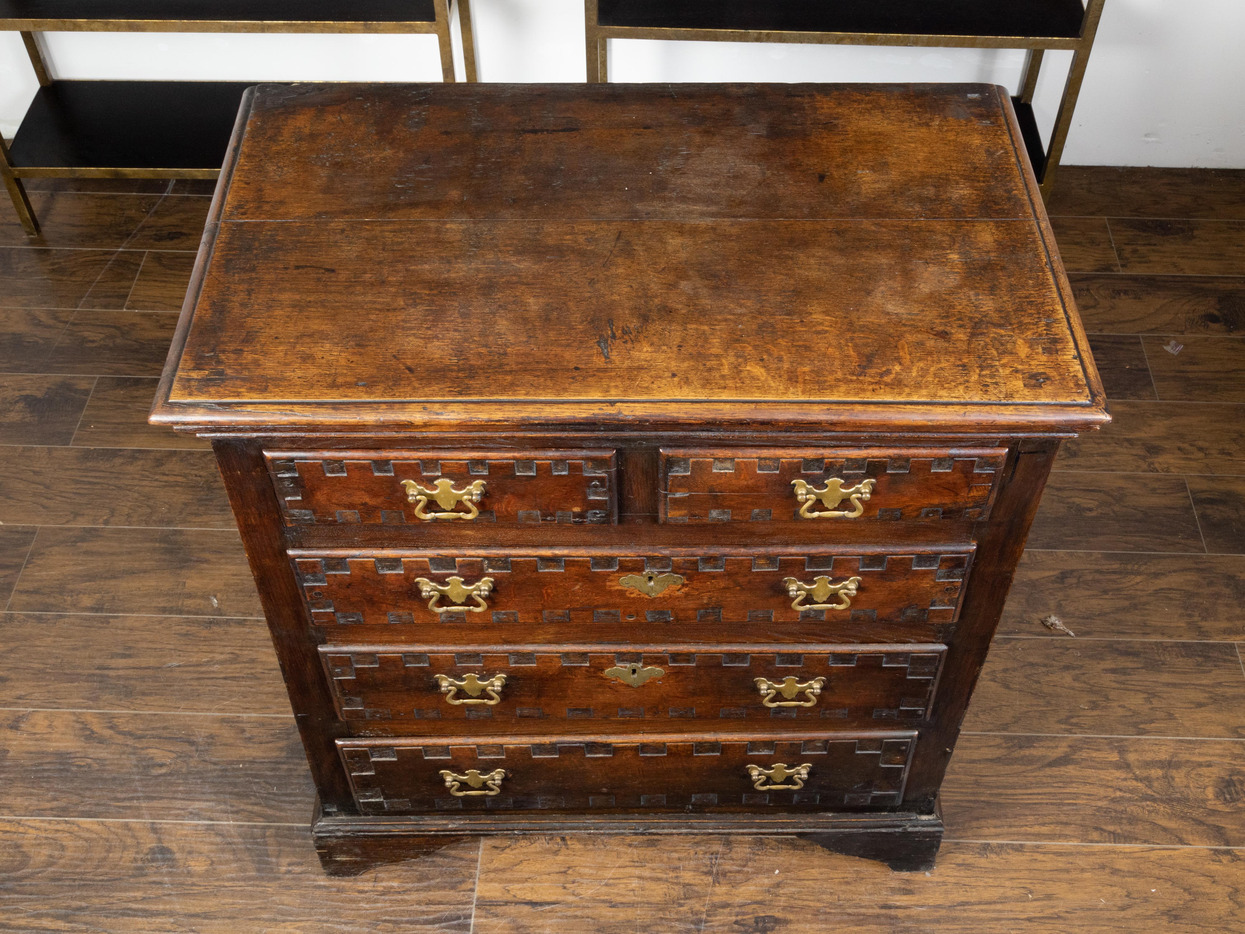 An English Georgian period oak chest from the early 19th century, with five drawers and carved square motifs. Created in England during the early years of the 19th century, this Georgian oak chest features a rectangular top with beveled edges,