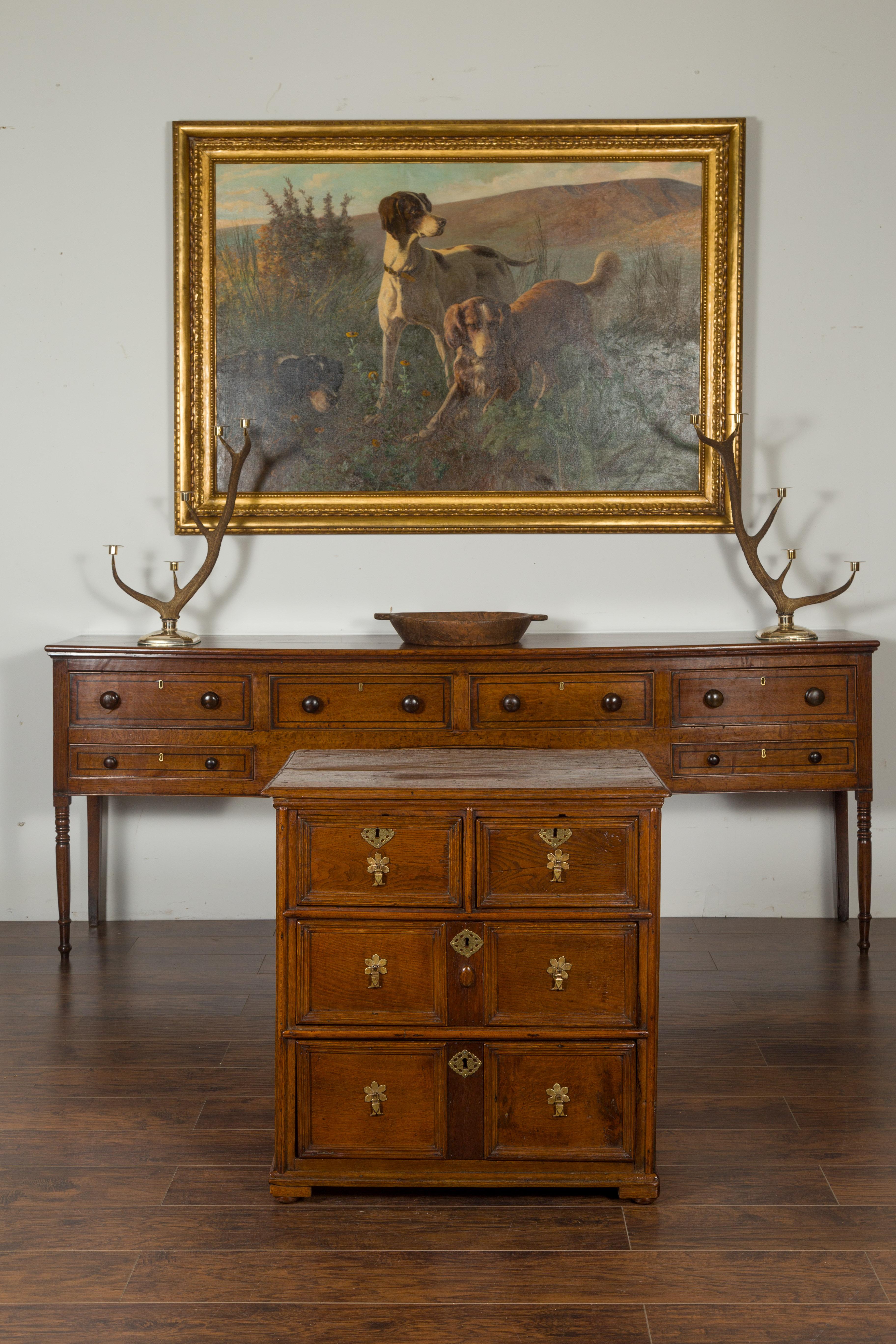 An English Georgian period oak four-drawer chest from the early 19th century, with floral brass hardware. Created in England during the first quarter of the 19th century, this Georgian oak chest features a rectangular top with beveled edges, sitting