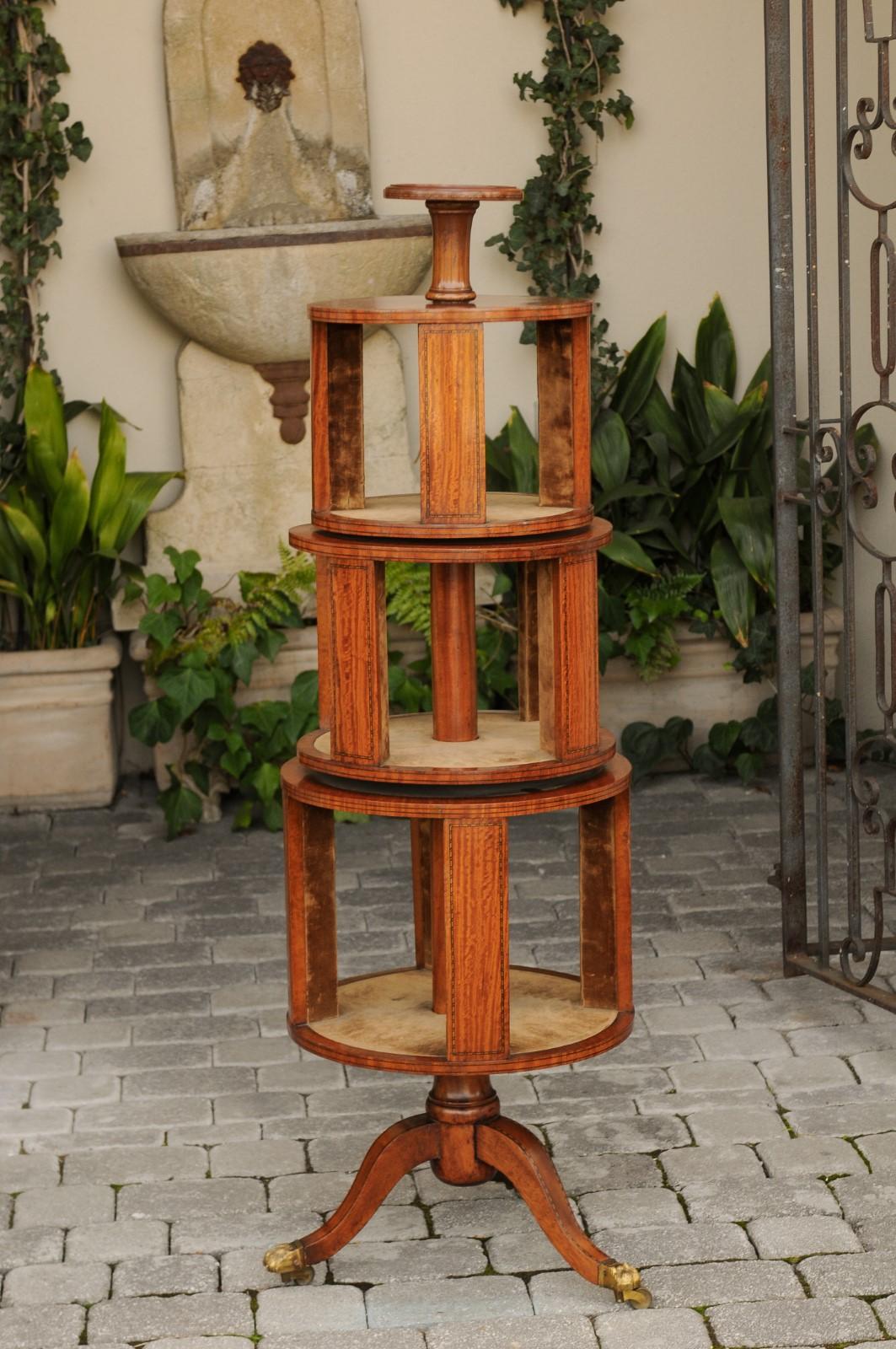 An English Georgian period mahogany tiered book revolving trolley on casters from the early 19th century, with suede lining, banding and tripod base. Born during the first quarter of the 19th century, this English circular book trolley features a