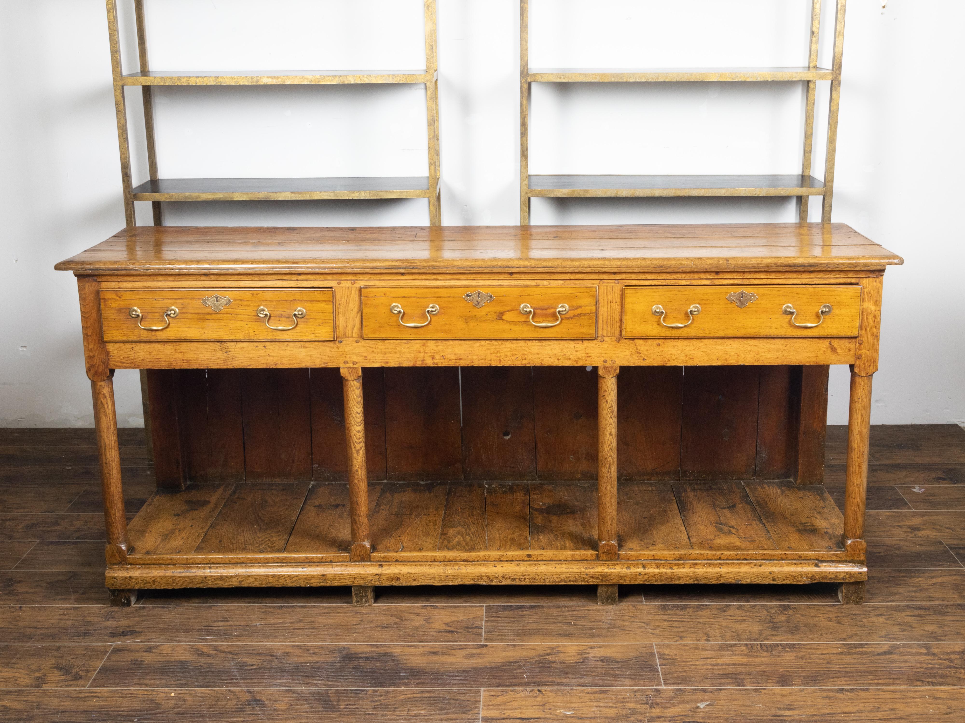 An English Georgian period dresser base from the early 19th century, with three drawers and pot board shelf. Created in England during the first quarter of the 19th century, this wooden dresser base features a rectangular planked top sitting above