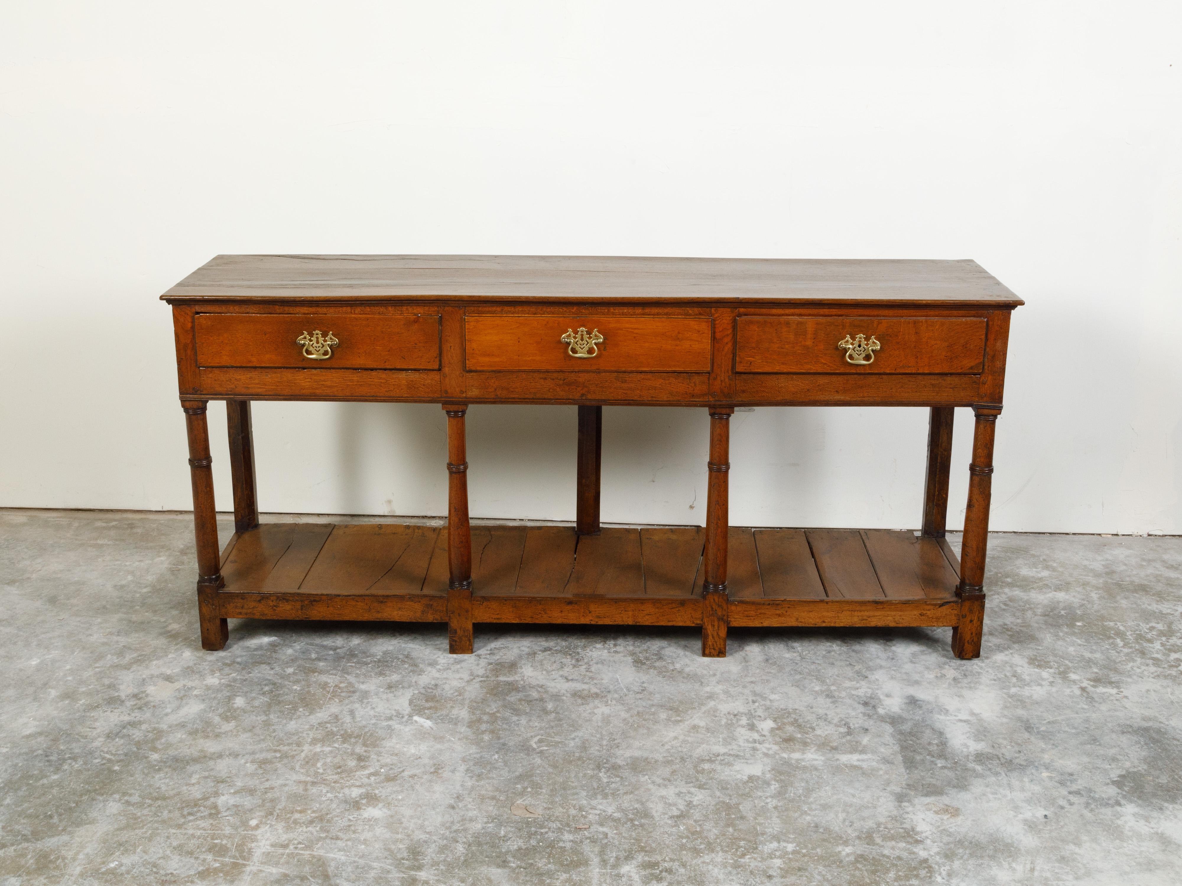 An English Georgian period oak dresser base from the early 19th century, with three drawers and pot board shelf. Created in England during the first quarter of the 19th century, this dresser base features a rectangular top sitting above three