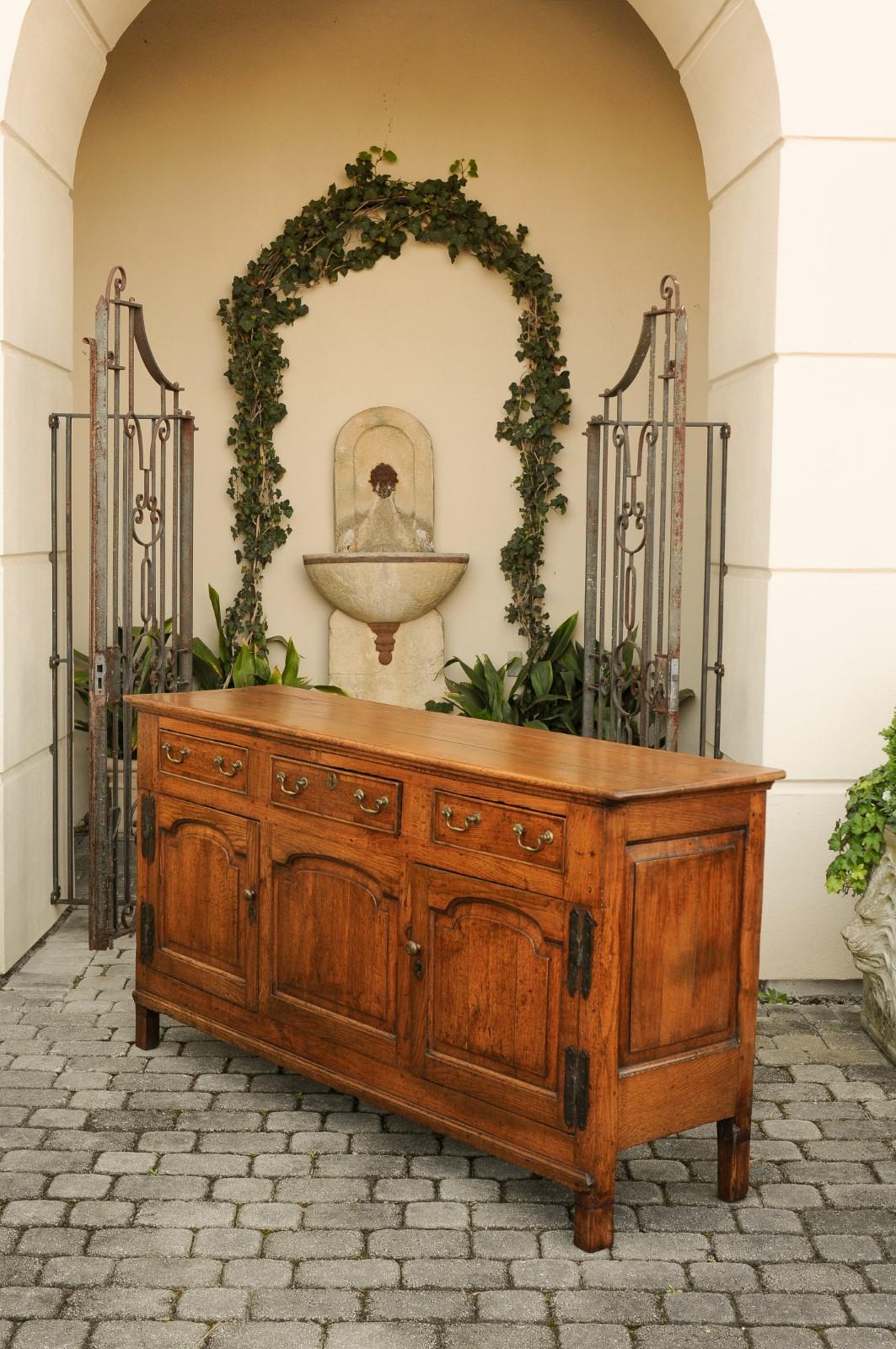 An English oak enfilade from the early 19th century, with three drawers over two doors, brass hardware and metal hinges. Born in England during the first quarter of the 19th century, this oak enfilade features a rectangular planked top sitting above