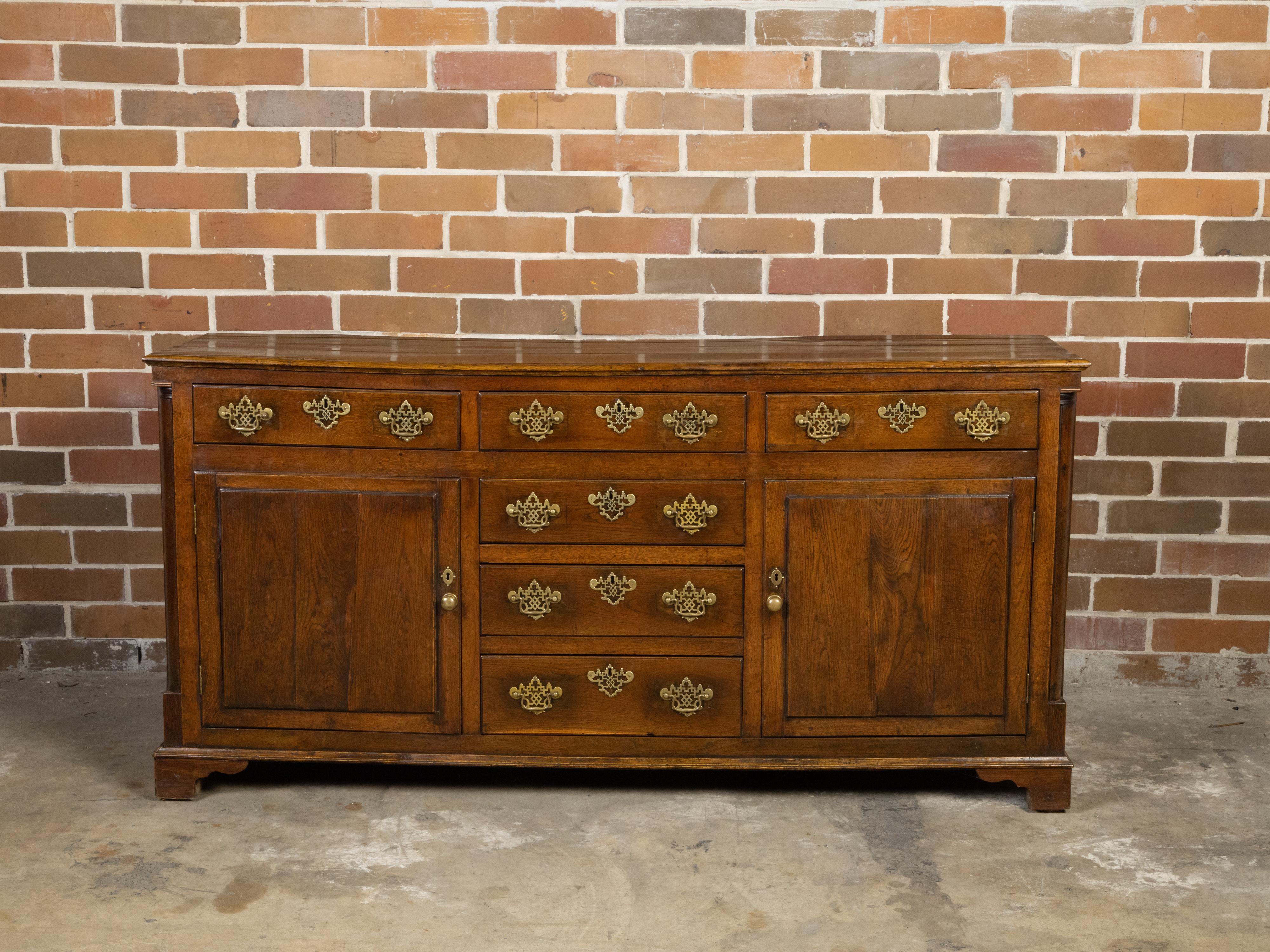 An English oak dresser base from the early 19th century with T-shaped drawers, semi Doric columns, two doors and brass Chippendale style hardware. Created in England during the first quarter of the 19th century, this oak dresser base features a